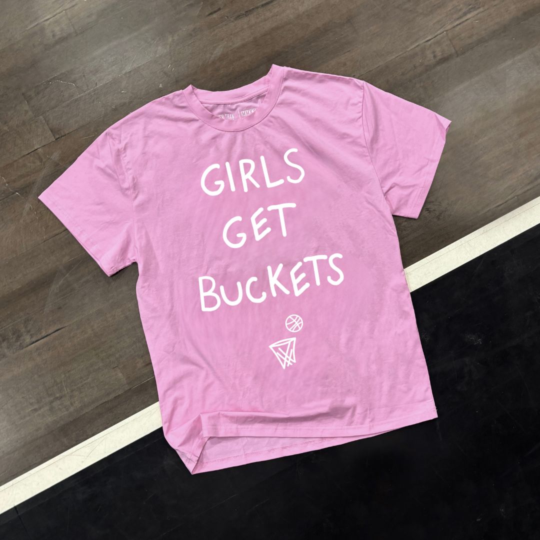 Pink t-shirt with 'GIRLS GET BUCKETS' text on a wooden floor.