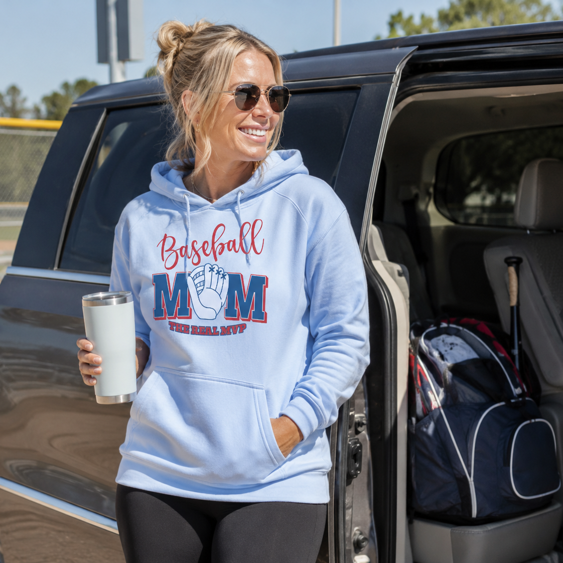 Collection of Woman in a 'Baseball Mom' hoodie standing next to an open car door, holding a tumbler. in a gallery layout