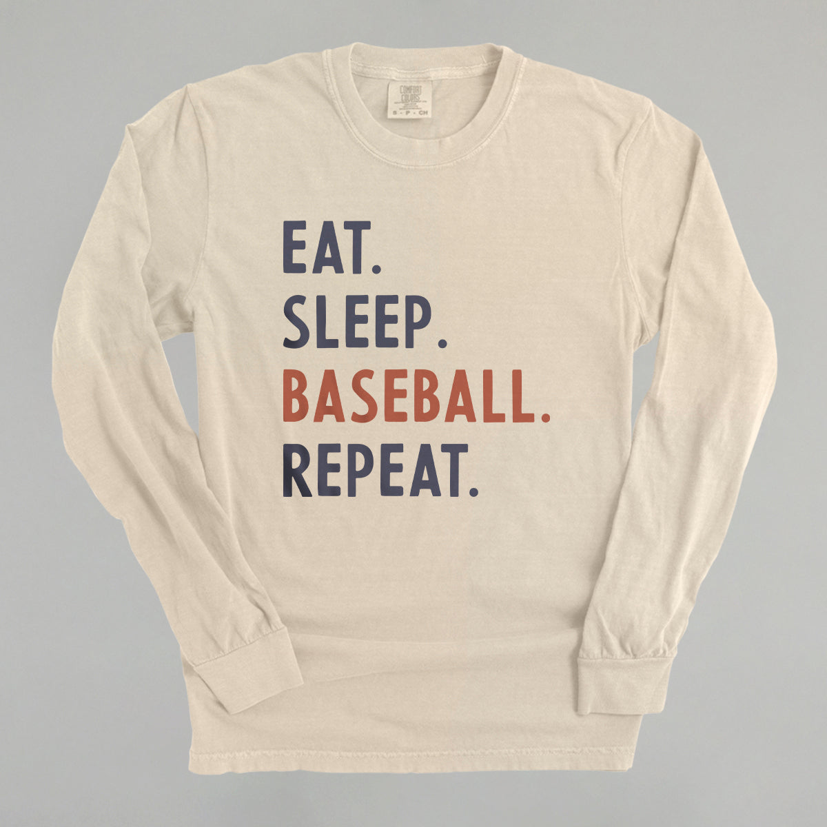 Beige long-sleeve shirt with 'Eat. Sleep. Baseball. Repeat.' text on a gray background
