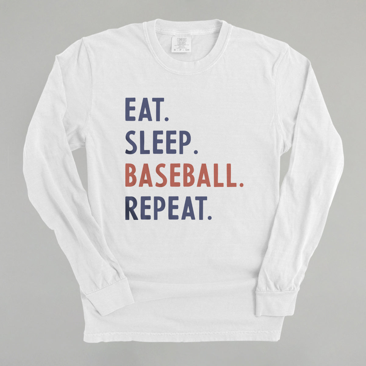 White long-sleeve shirt with 'Eat. Sleep. Baseball. Repeat.' text on a gray background