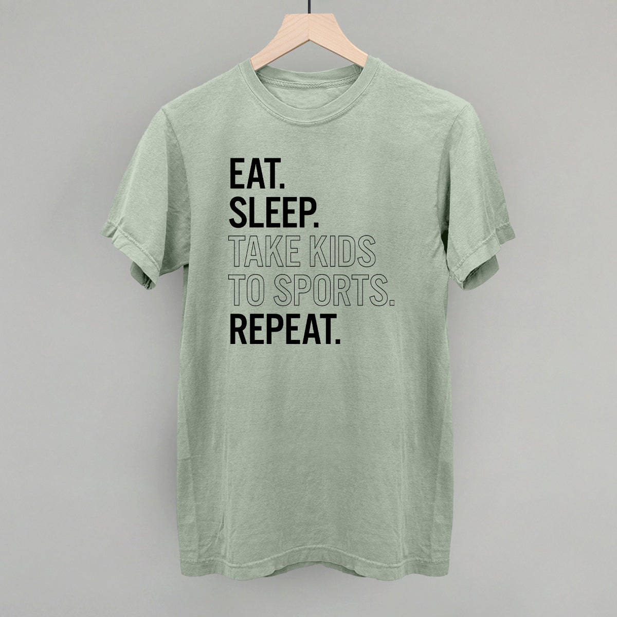 Collection of Green comfort colors t-shirt with text 'Eat. Sleep. Take kids to sports. Repeat.' on a gray background in a gallery layout