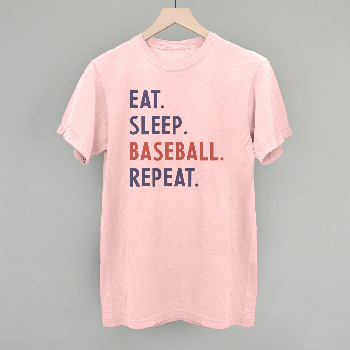 Pink t-shirt with 'Eat. Sleep. Baseball. Repeat.' text on a gray background