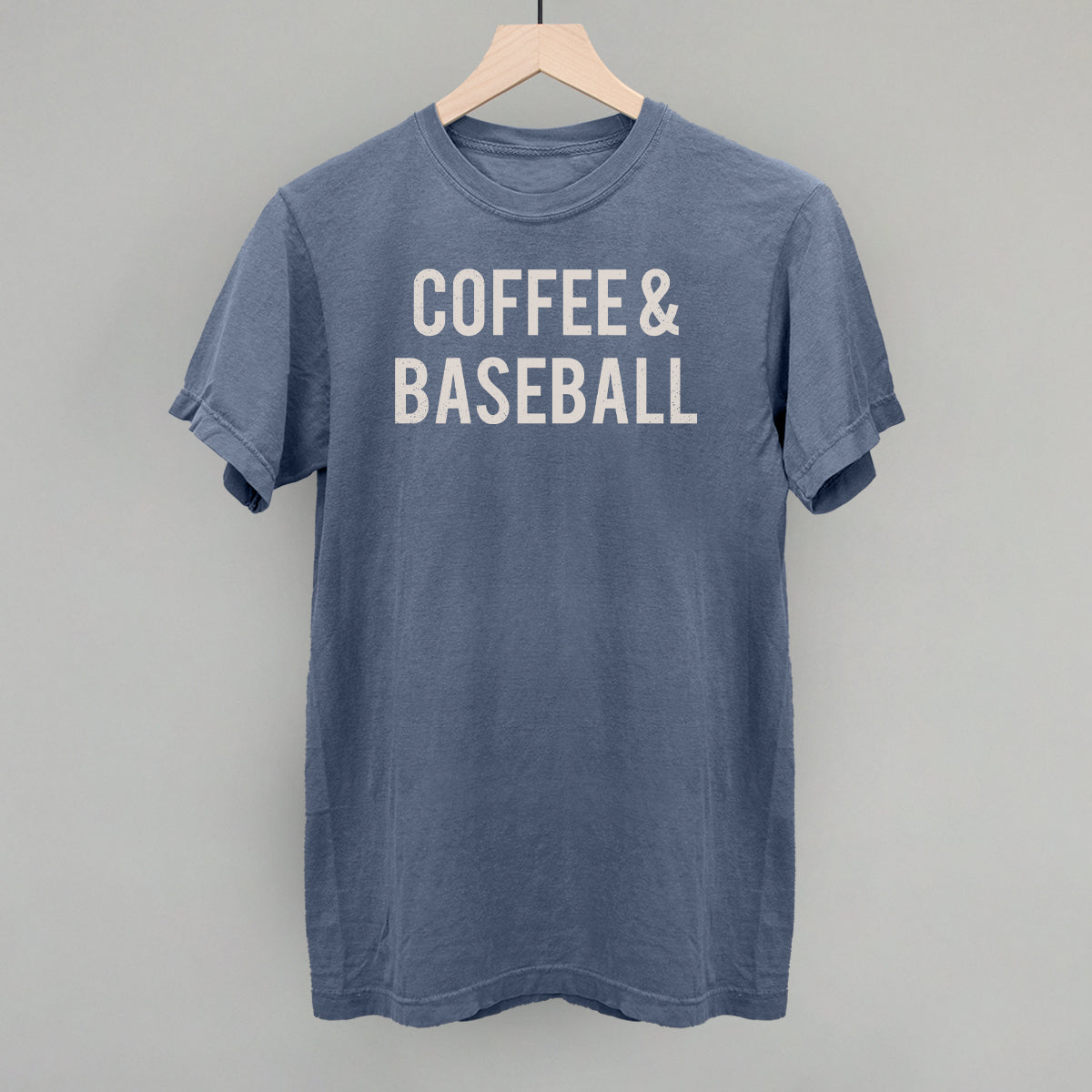 Blue comfort colors t-shirt with 'COFFEE & BASEBALL' text on a hanger against a gray background