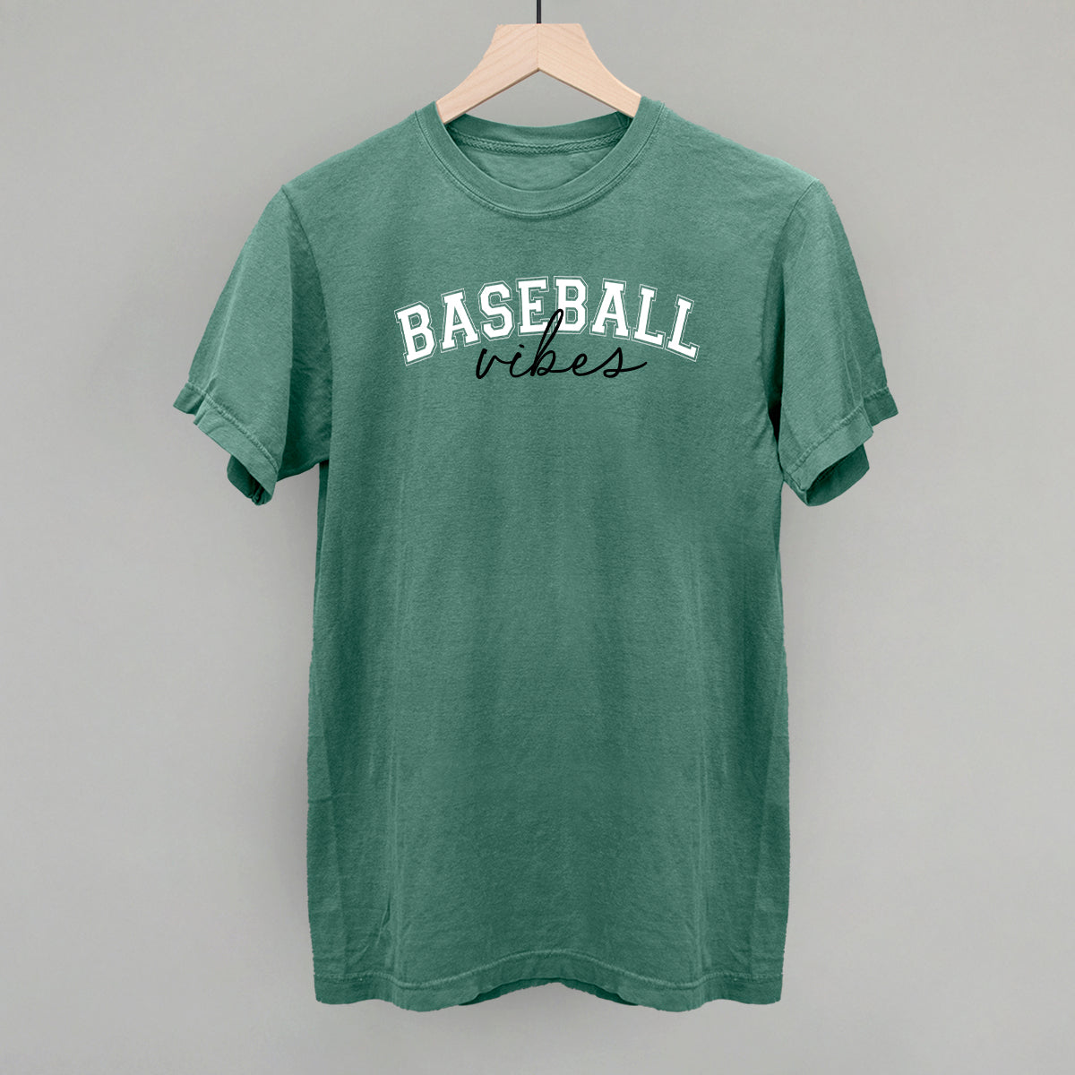 Green t-shirt with 'BASEBALL vibes' text on a wooden hanger against a gray background