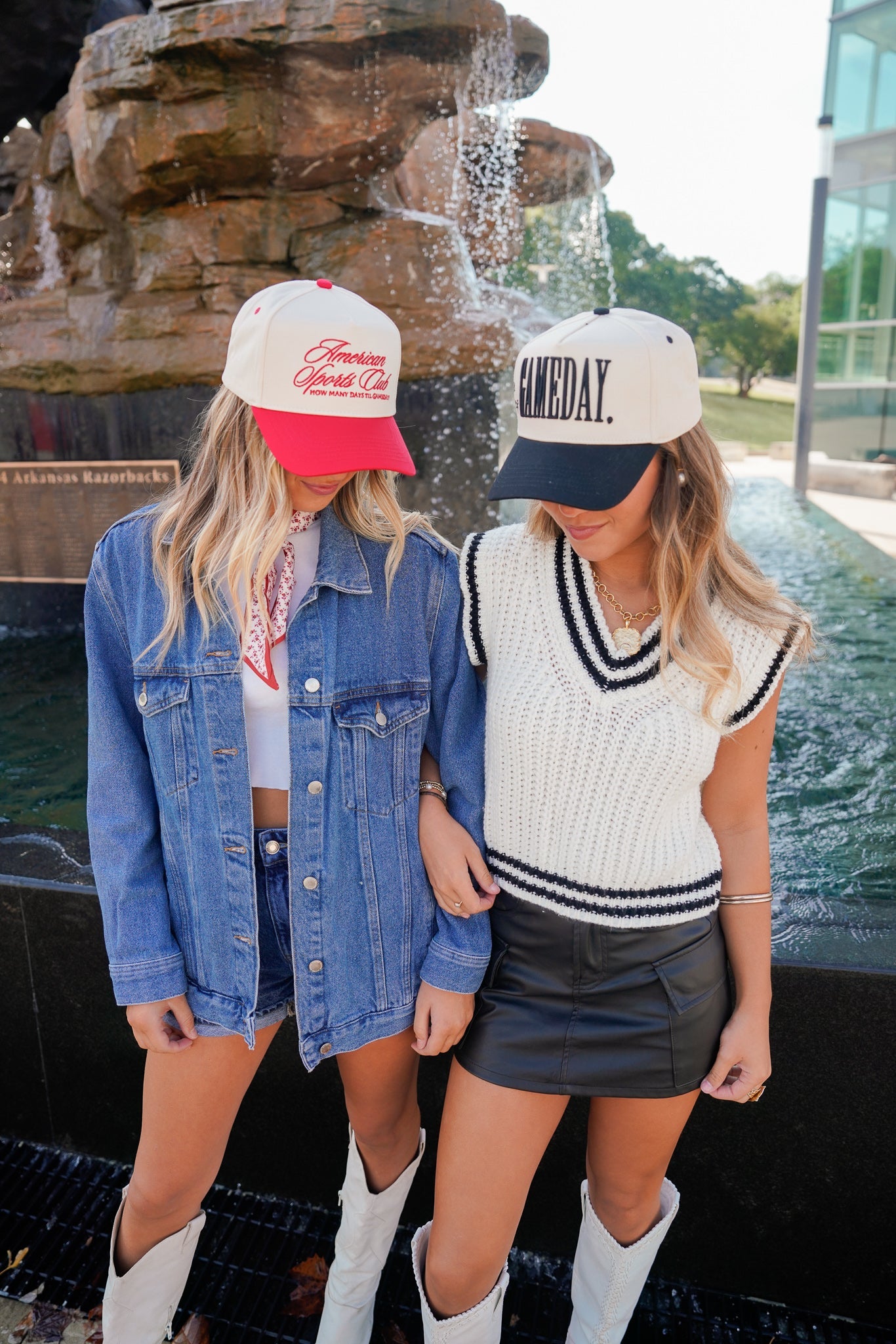Two women standing in front of a fountain, wearing casual outfits with hats.