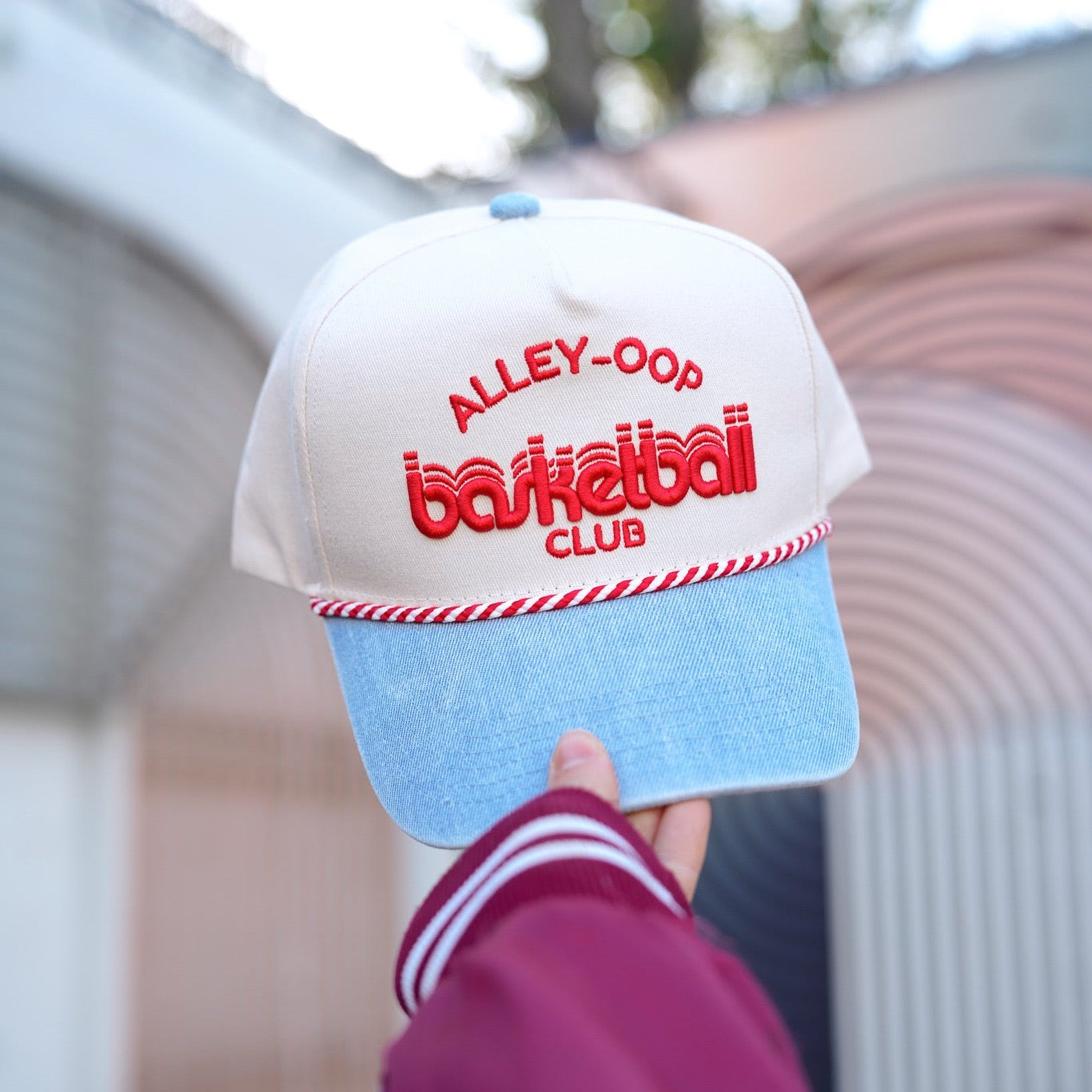 Cap with 'Alley-Oop Basketball Club' text held by a person wearing a maroon jacket.