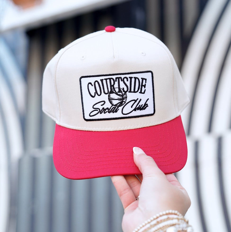 Collection of Hand holding a red and white cap with 'Courtside Social Club' logo against a blurred outdoor background. in a gallery layout