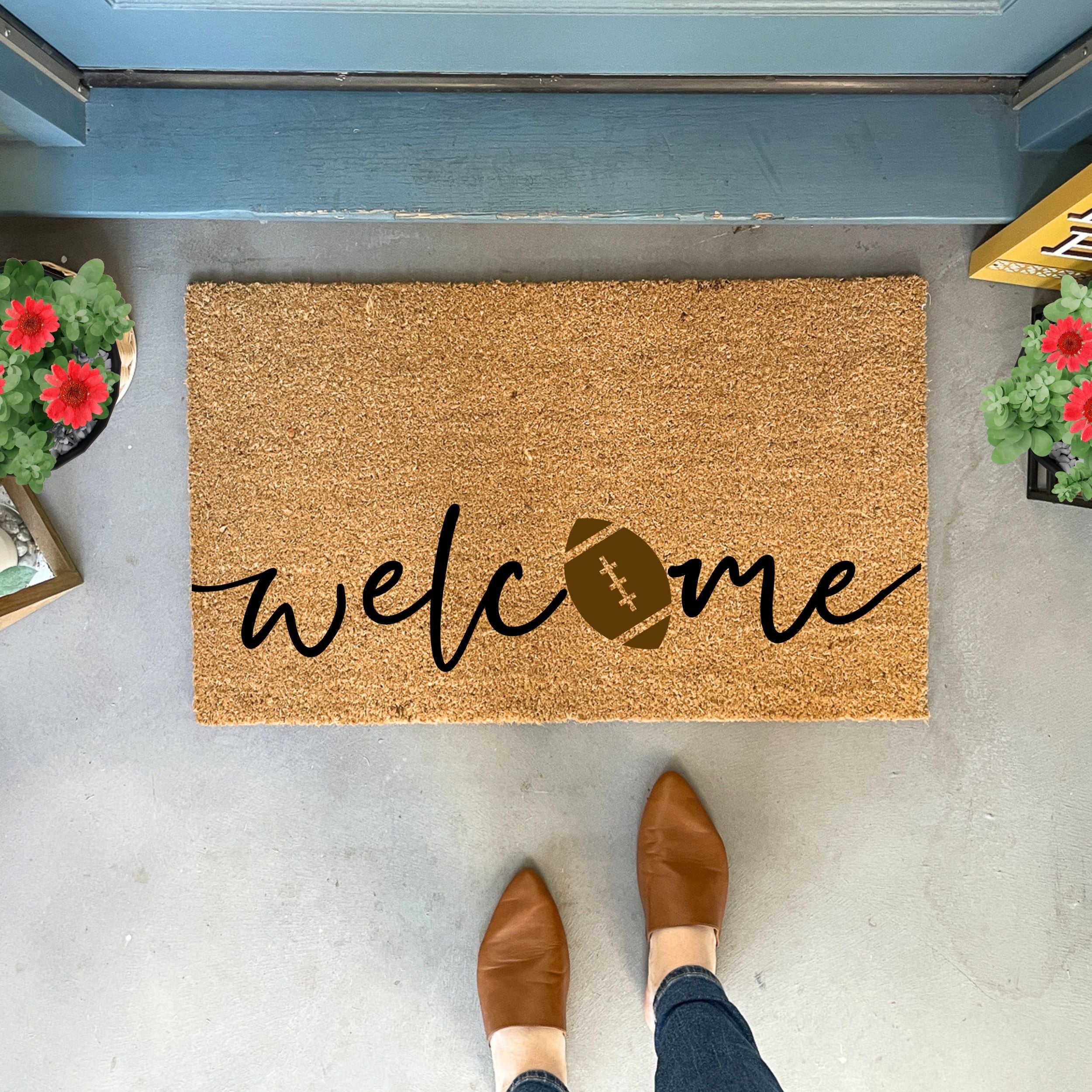 Collection of Doormat with 'welcome' and football design on a concrete floor, with shoes and plants visible. in a gallery layout