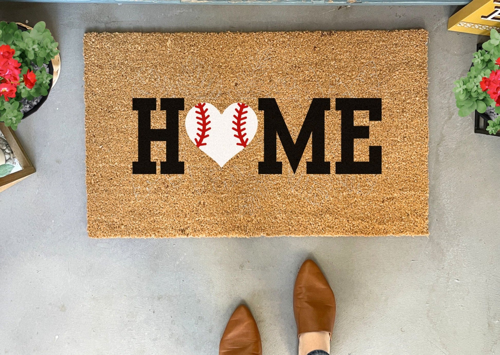 Doormat with 'HOME' text and baseball heart design on a concrete floor.