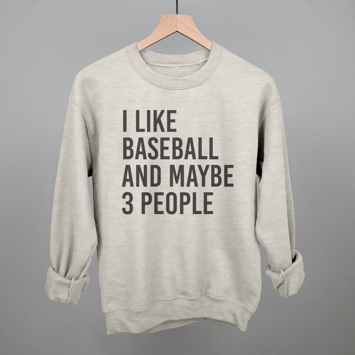 Collection of oatmeal color sweatshirt with 'I like baseball and maybe 3 people' text on a hanger against a gray background in a gallery layout