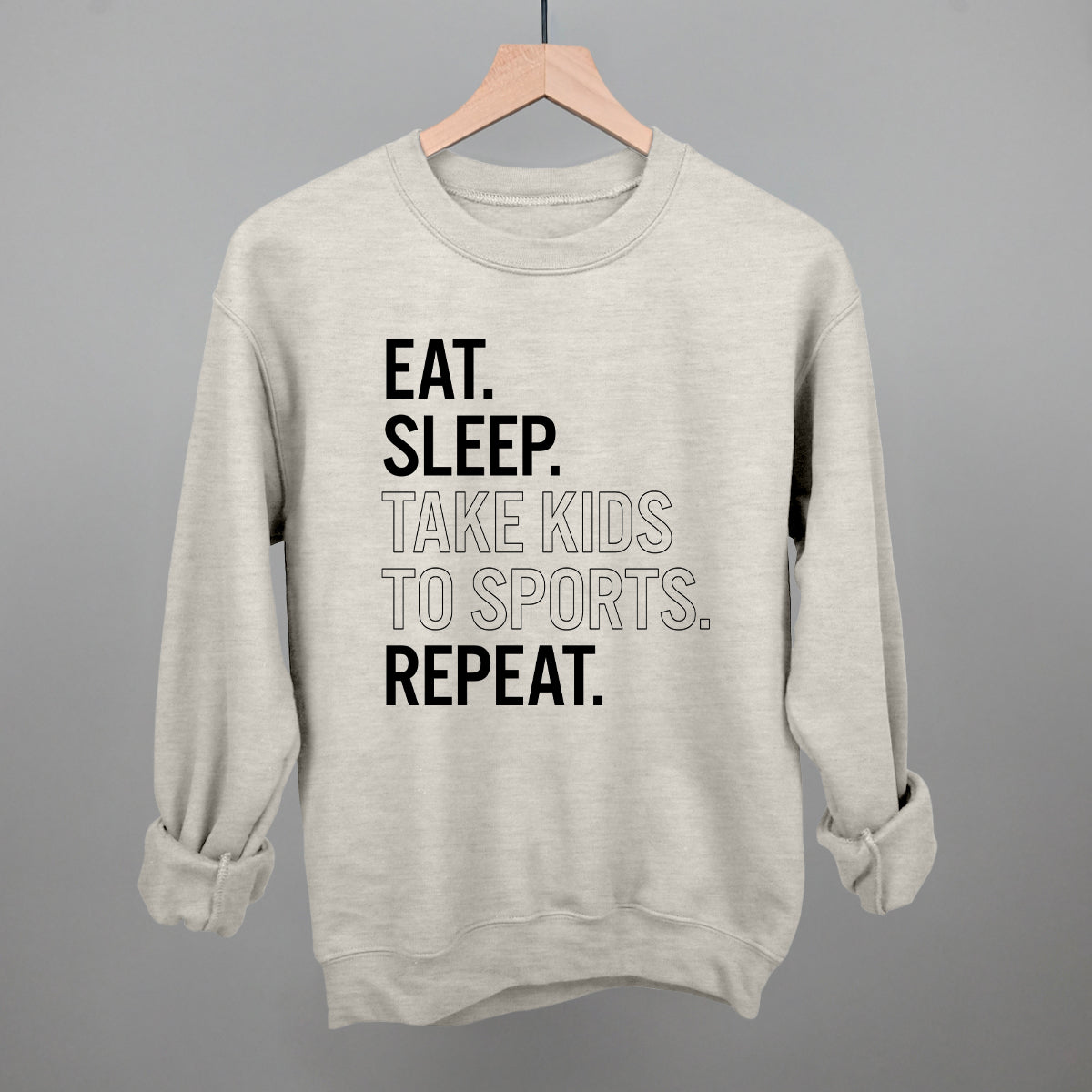 oatmeal comfort colors sweatshirt with text 'EAT. SLEEP. TAKE KIDS TO SPORTS. REPEAT.' on a gray background