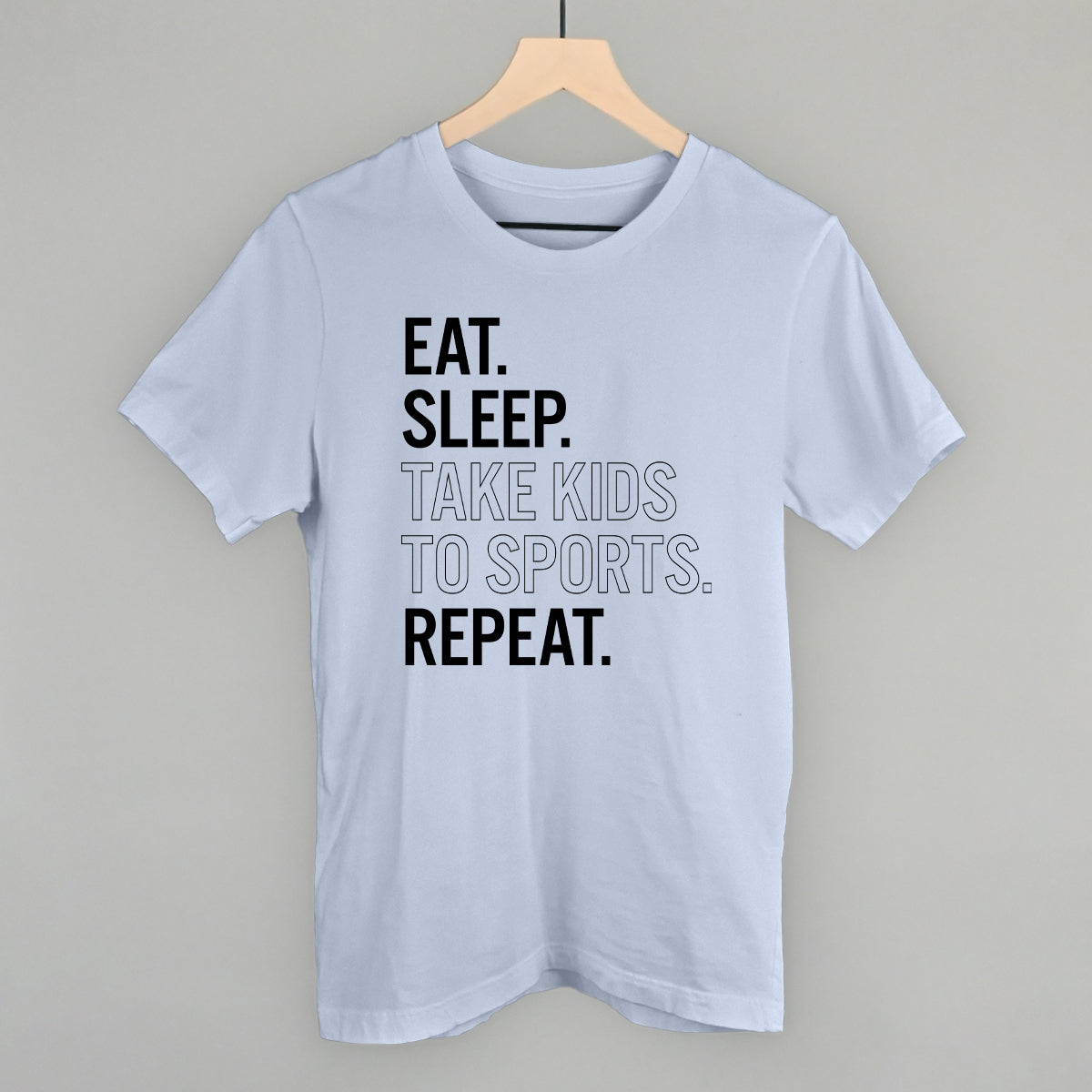 Collection of Light blue comfort color t-shirt with text 'EAT. SLEEP. TAKE KIDS TO SPORTS. REPEAT.' on a hanger against a gray background in a gallery layout