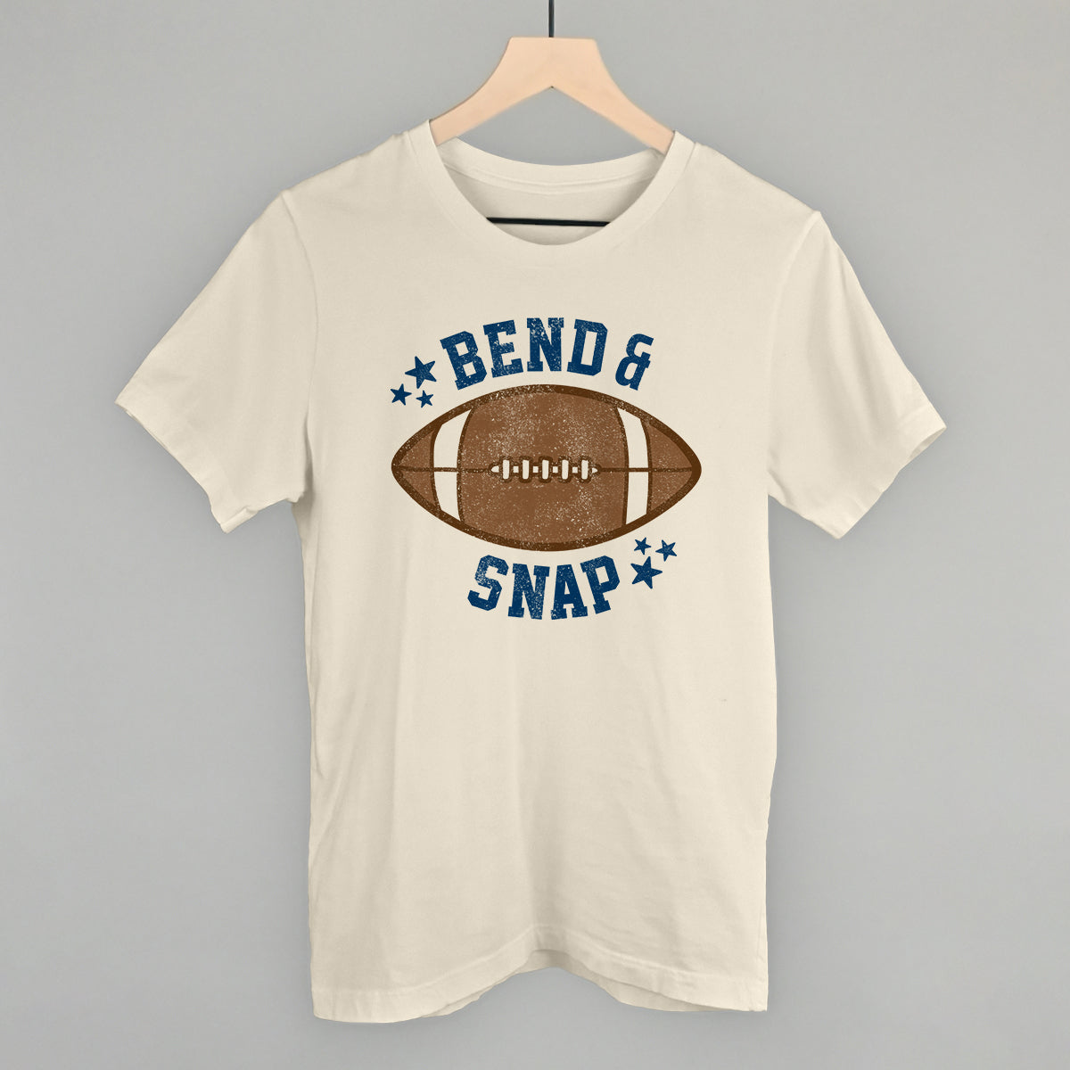 Beige t-shirt with football graphic and text 'Bend & Snap' on a gray background