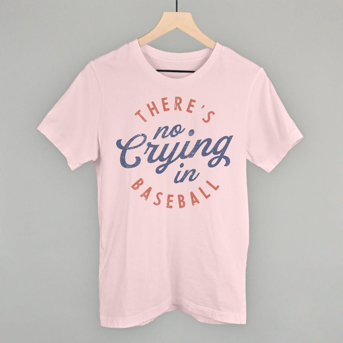 Collection of Pink t-shirt with 'There's no crying in baseball' text on a hanger against a gray background in a gallery layout