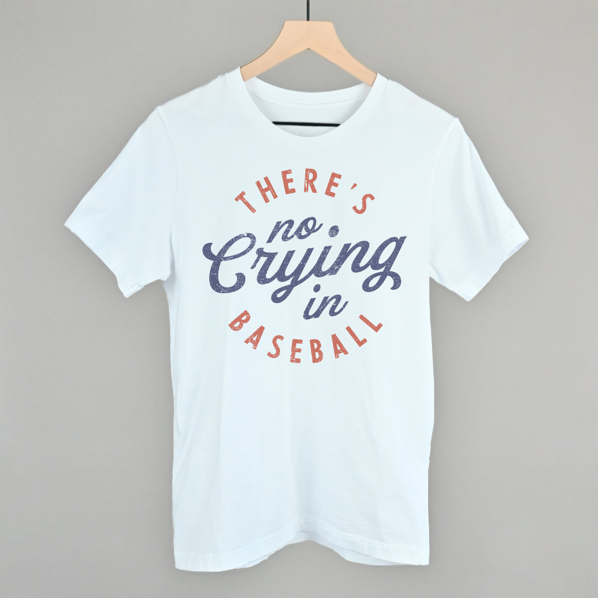 Collection of White t-shirt with 'There's no crying in baseball' text on a hanger against a gray background in a gallery layout