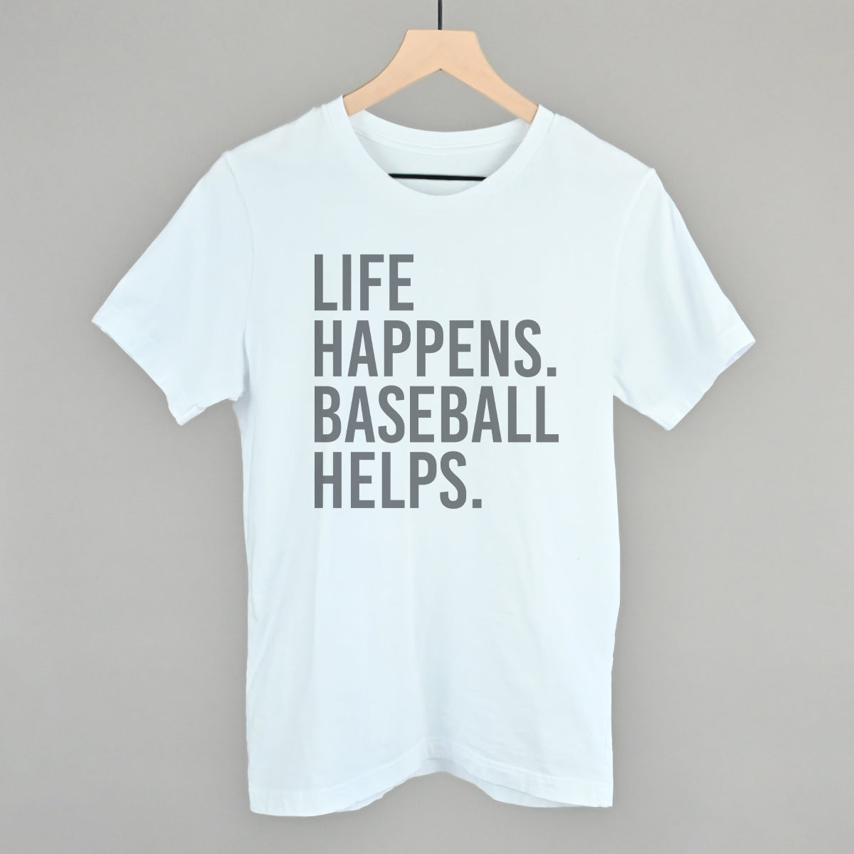 Collection of White t-shirt with 'Life happens. Baseball helps.' text on a hanger against a gray background in a gallery layout