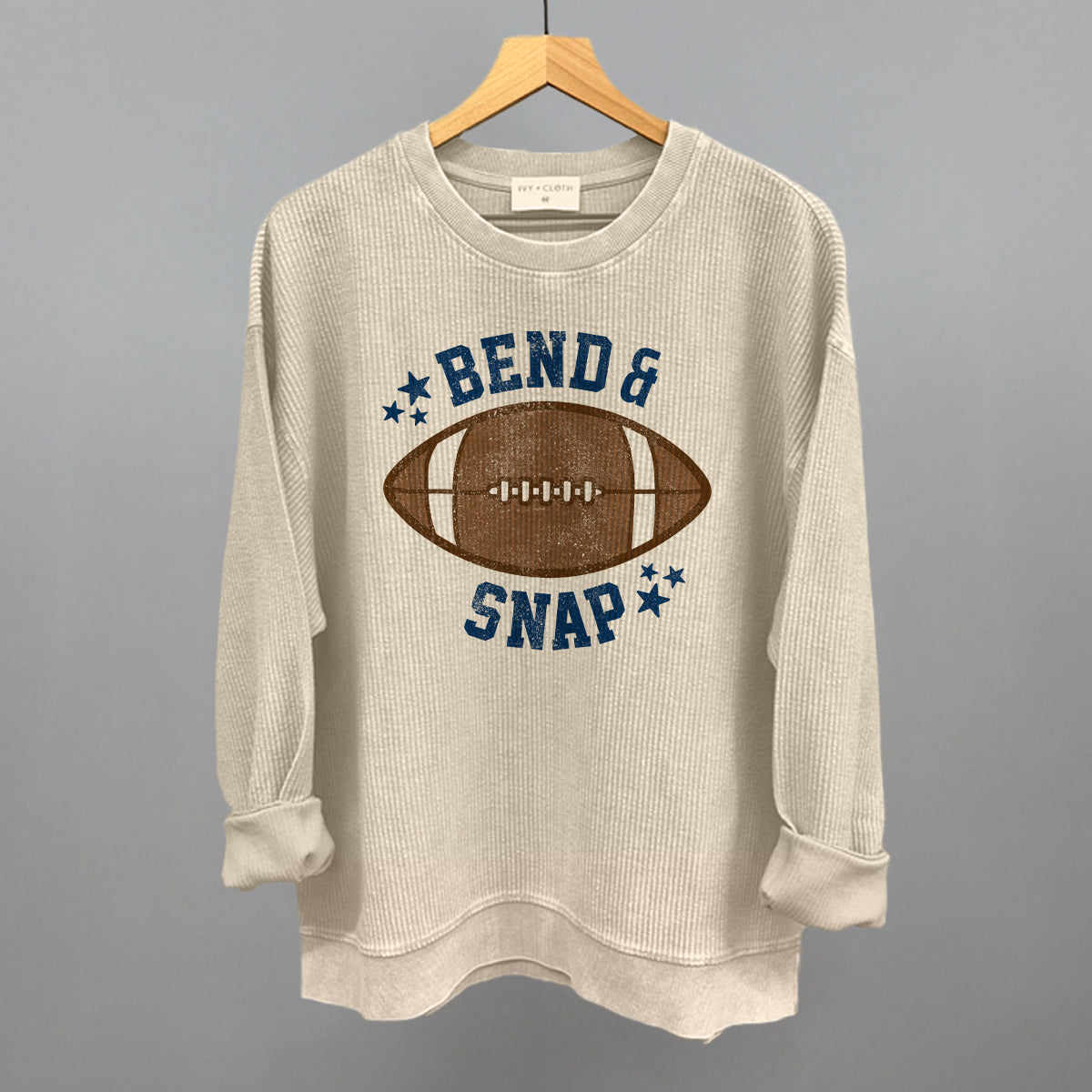 Beige sweatshirt with football graphic and text on a hanger against a gray background