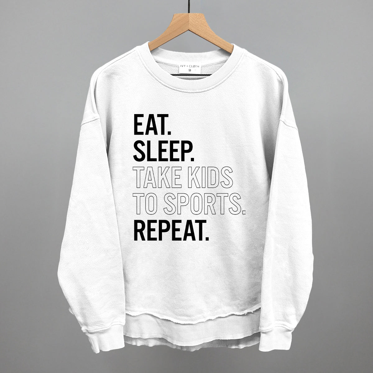 Collection of White sweatshirt with text 'EAT. SLEEP. TAKE KIDS TO SPORTS. REPEAT.' on a hanger against a gray background in a gallery layout