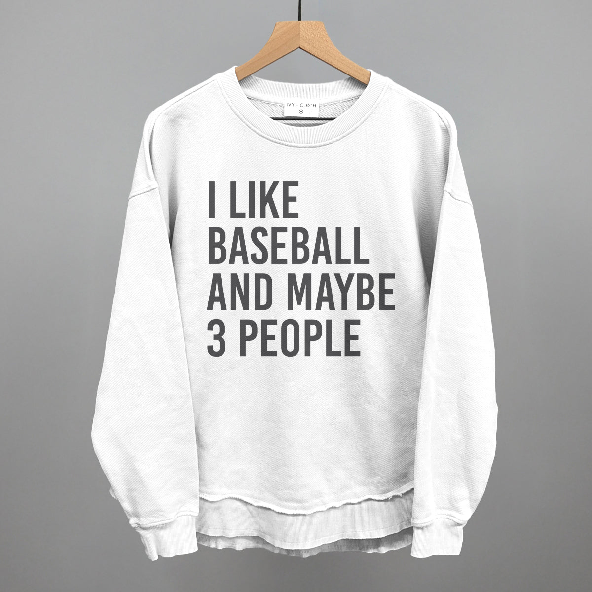 White sweatshirt with text 'I LIKE BASEBALL AND MAYBE 3 PEOPLE' on a hanger against a gray background