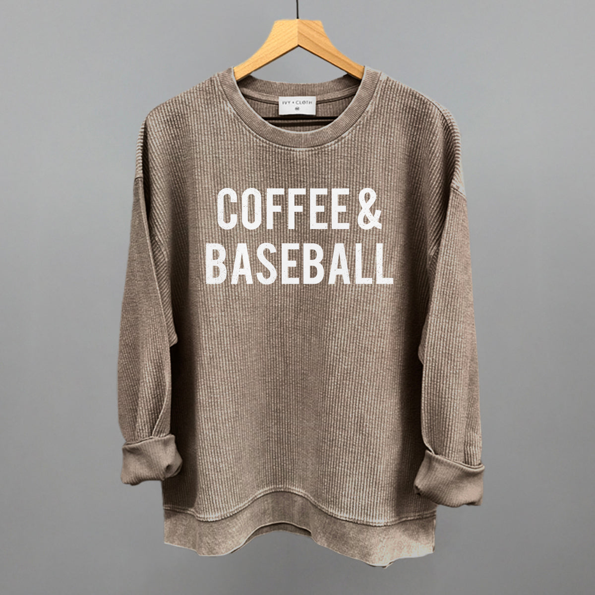 Brown corded crew sweatshirt with 'COFFEE & BASEBALL' text on a hanger against a gray background