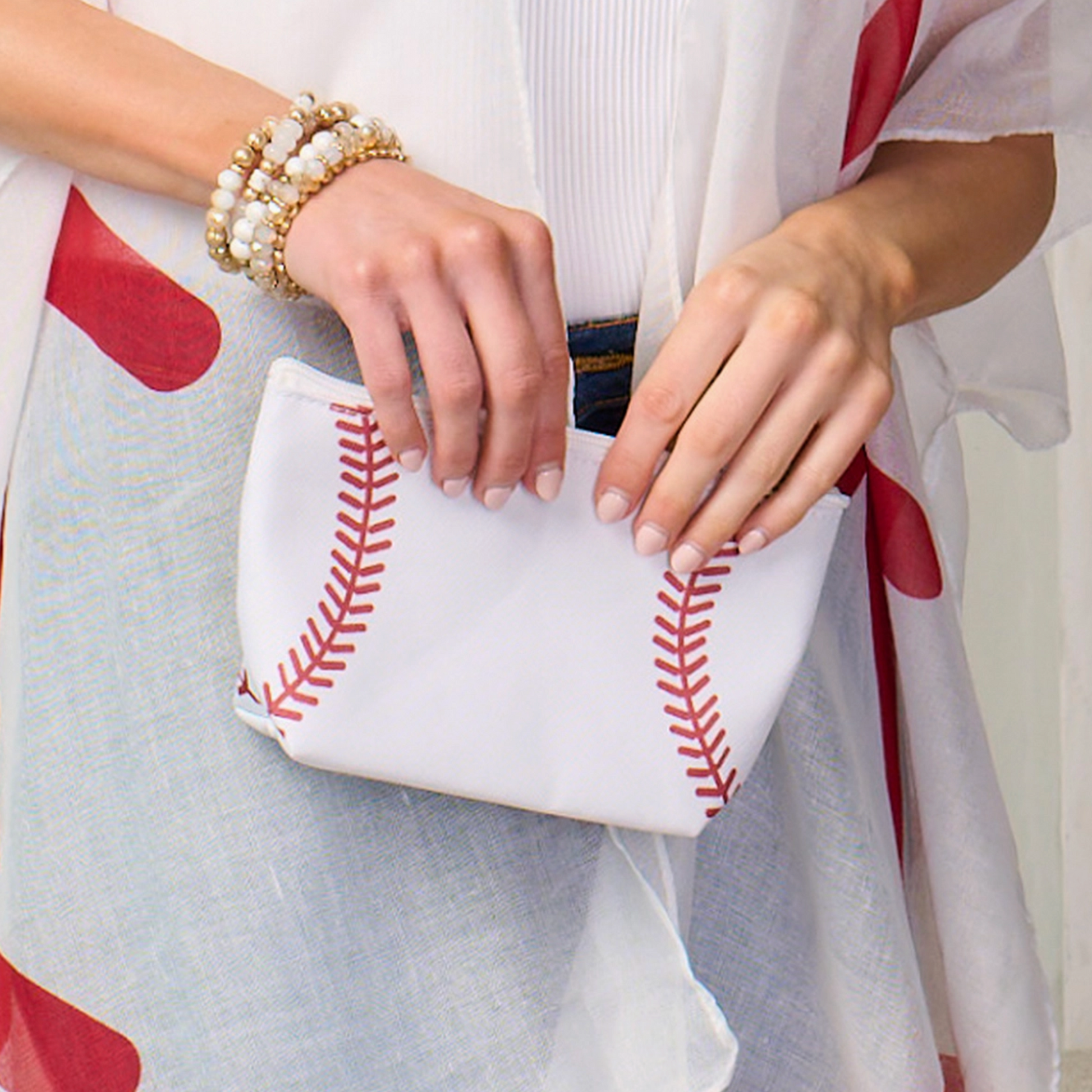 Person holding a white clutch with red stitching, wearing a white outfit with red accents.