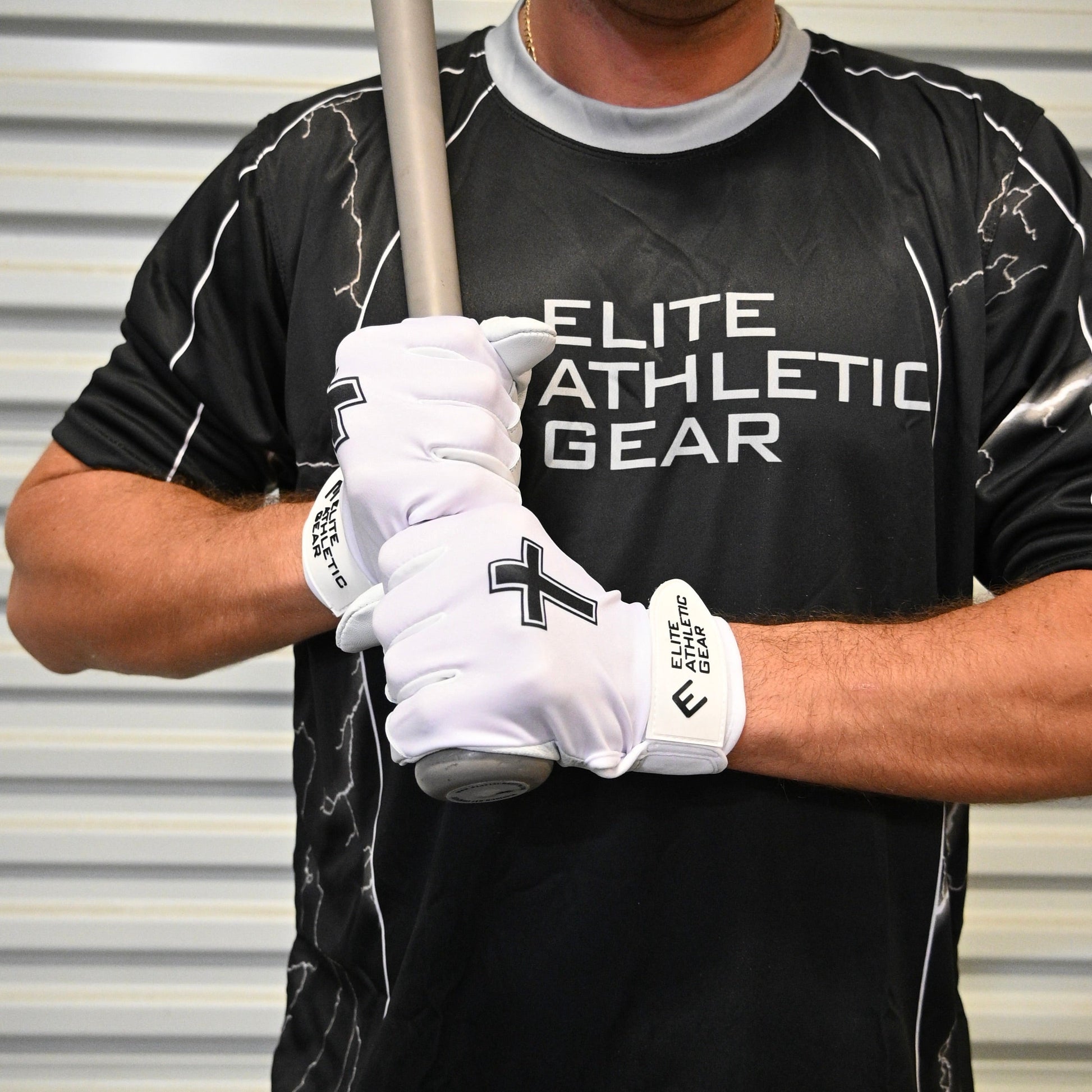 Person wearing a black 'Elite Athletic Gear' shirt and white gloves holding a baseball bat.
