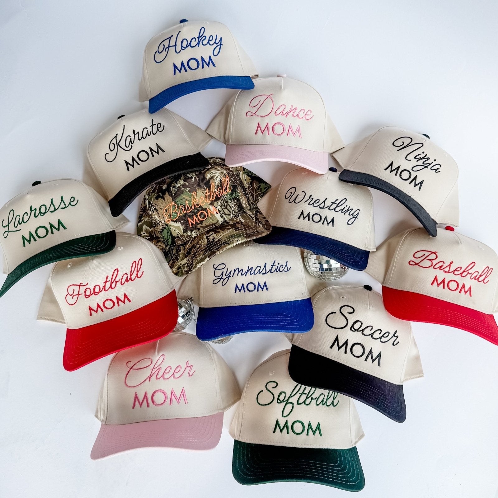 Collection of 'Mom' themed baseball caps with various sports text on a white background