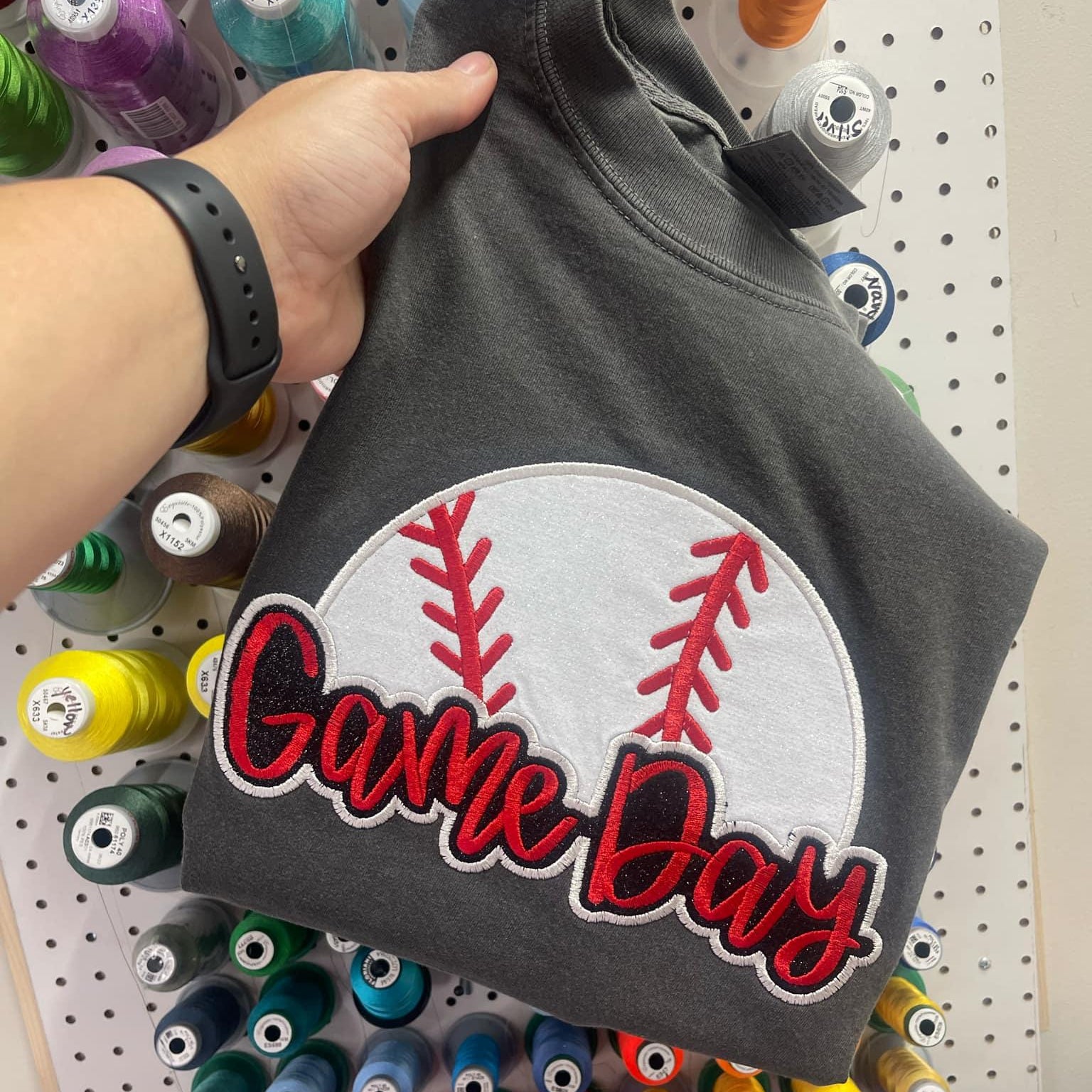 Collection of Gray sweatshirt with 'Game Day' patch held in front of a pegboard with spools of thread. in a gallery layout