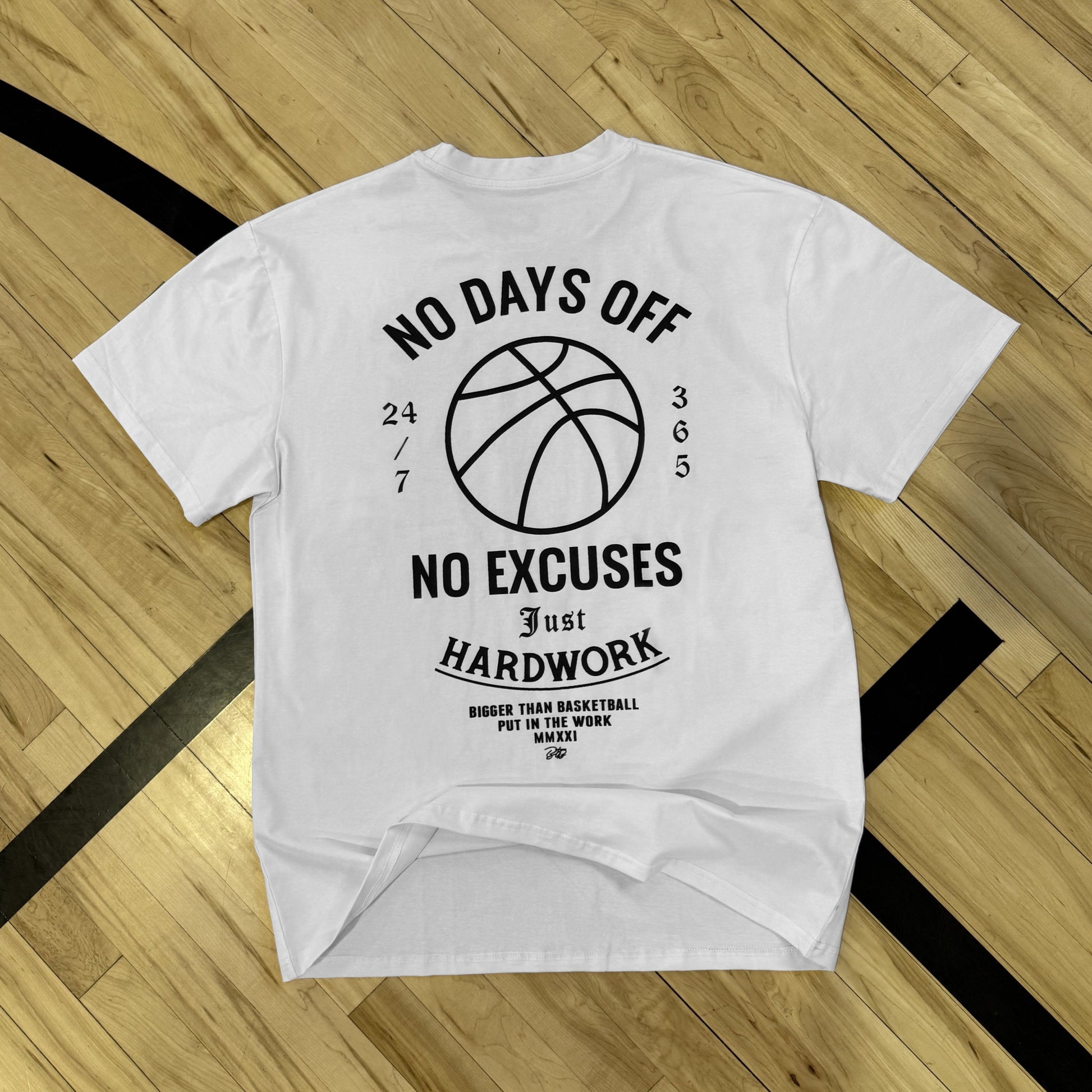 White t-shirt with black text and basketball graphic on a wooden floor background