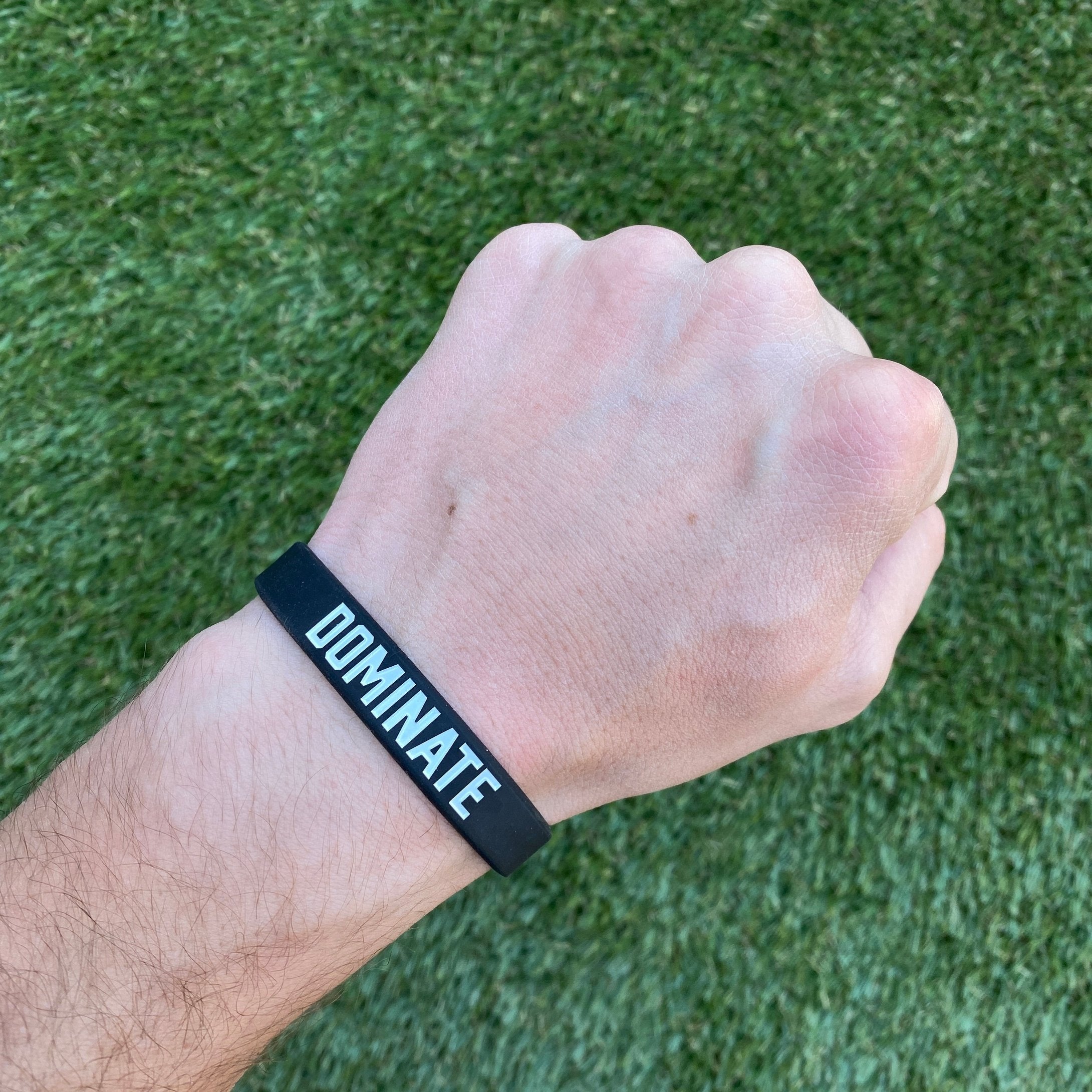 Collection of Hand wearing a black wristband with 'DOMINATE' text on a grass background in a gallery layout