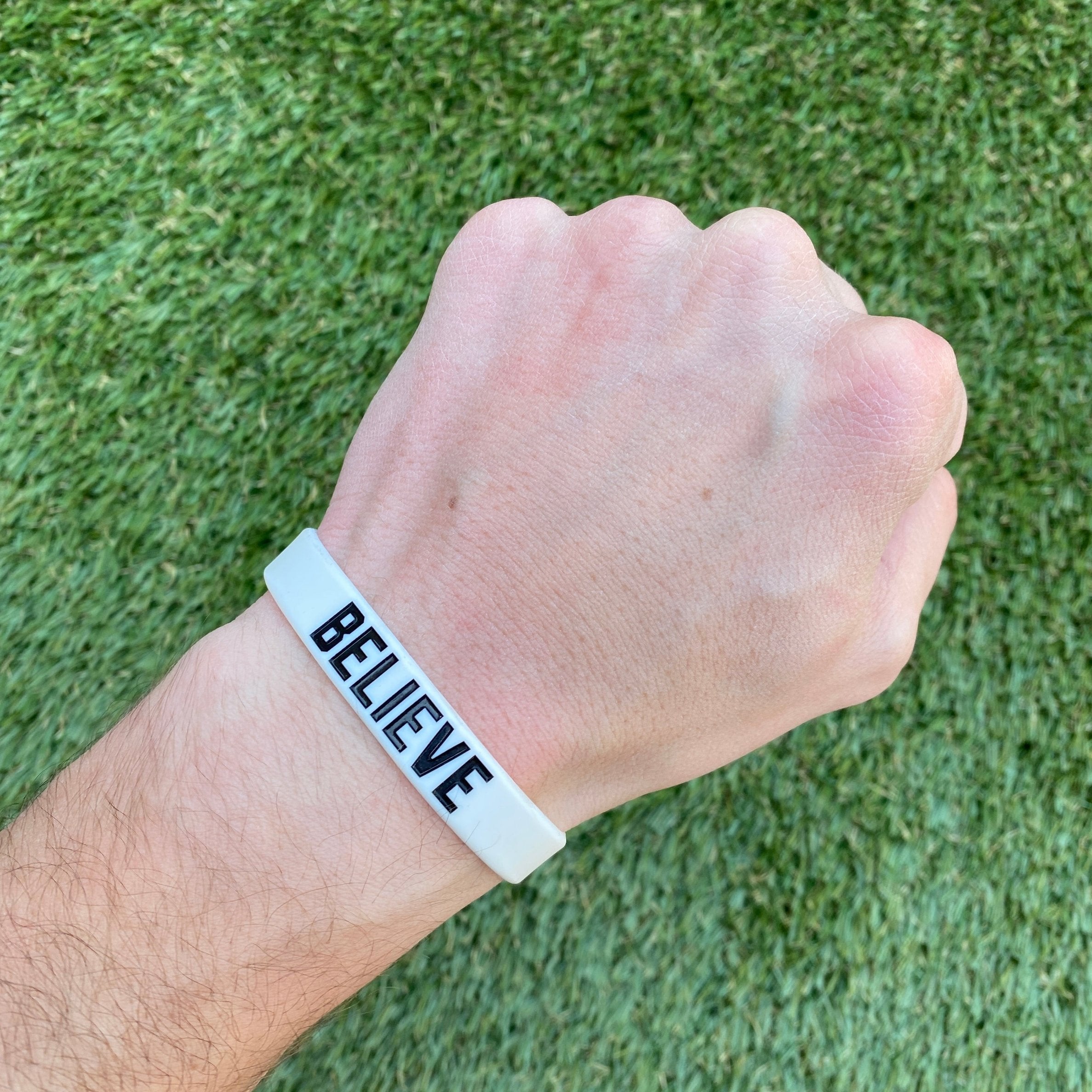 Collection of Hand wearing a white wristband with 'BELIEVE' text on a grass background in a gallery layout