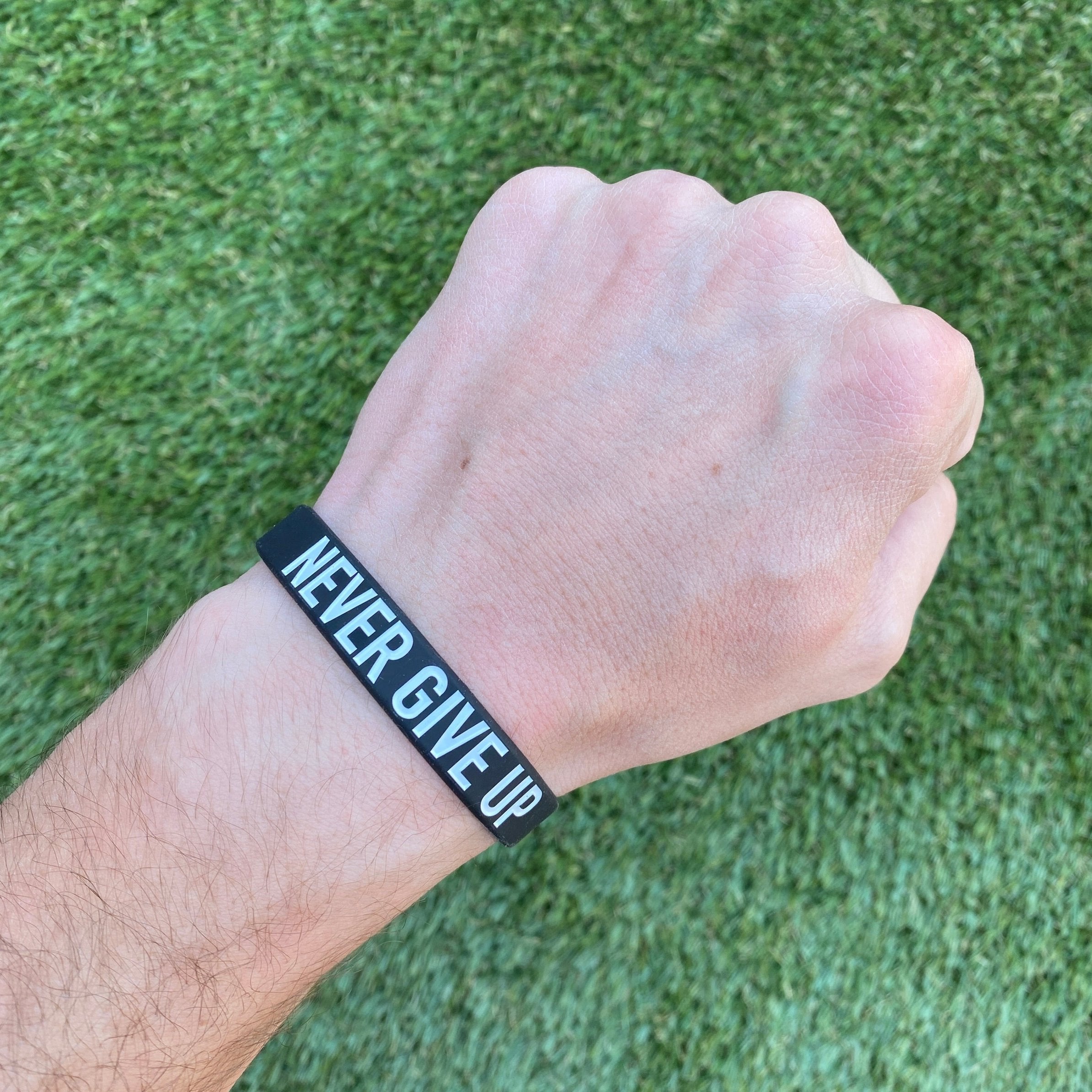 Collection of Hand wearing a black wristband with 'NEVER GIVE UP' text on a grass background in a gallery layout