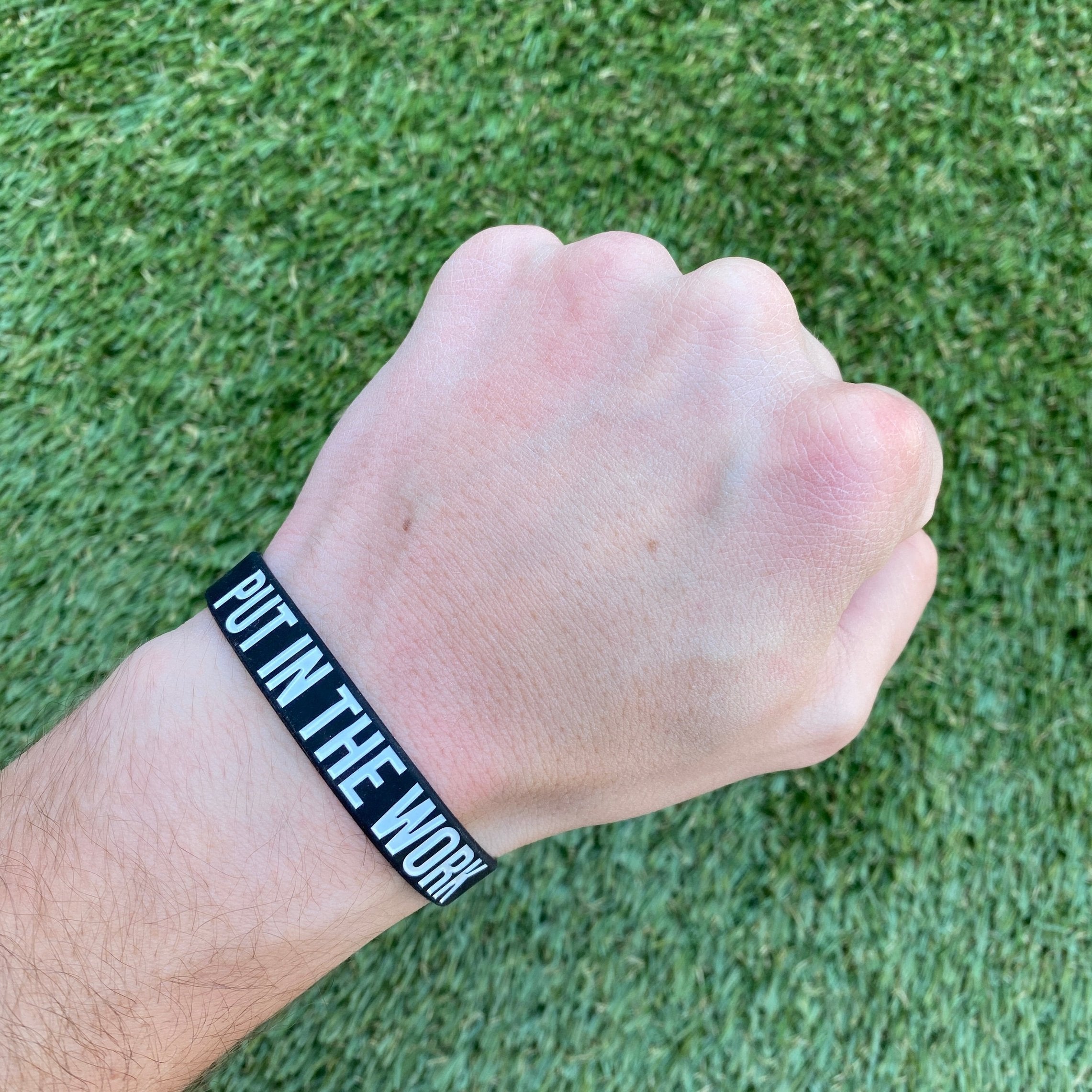 Collection of Hand wearing a black wristband with 'Put In The Work' text on a grass background in a gallery layout