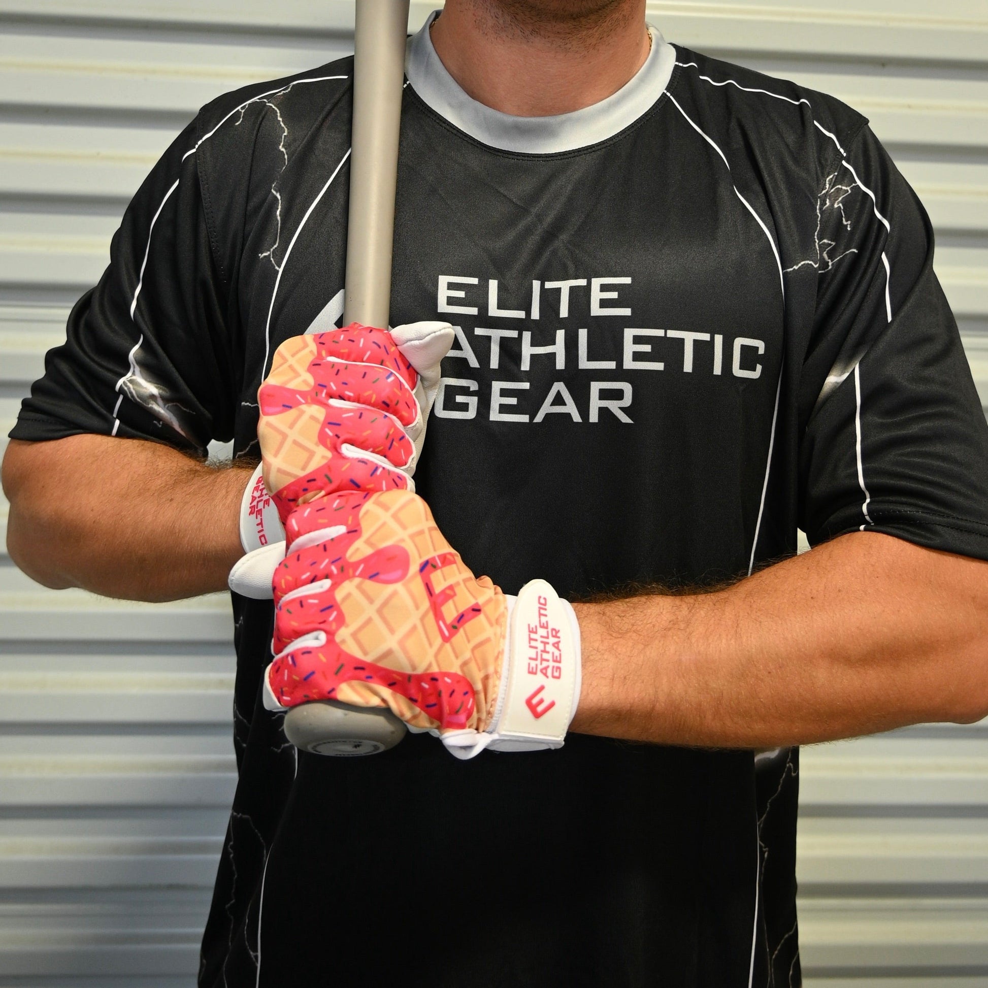 Person wearing a black 'Elite Athletic Gear' shirt holding a baseball bat with pink and white gloves.