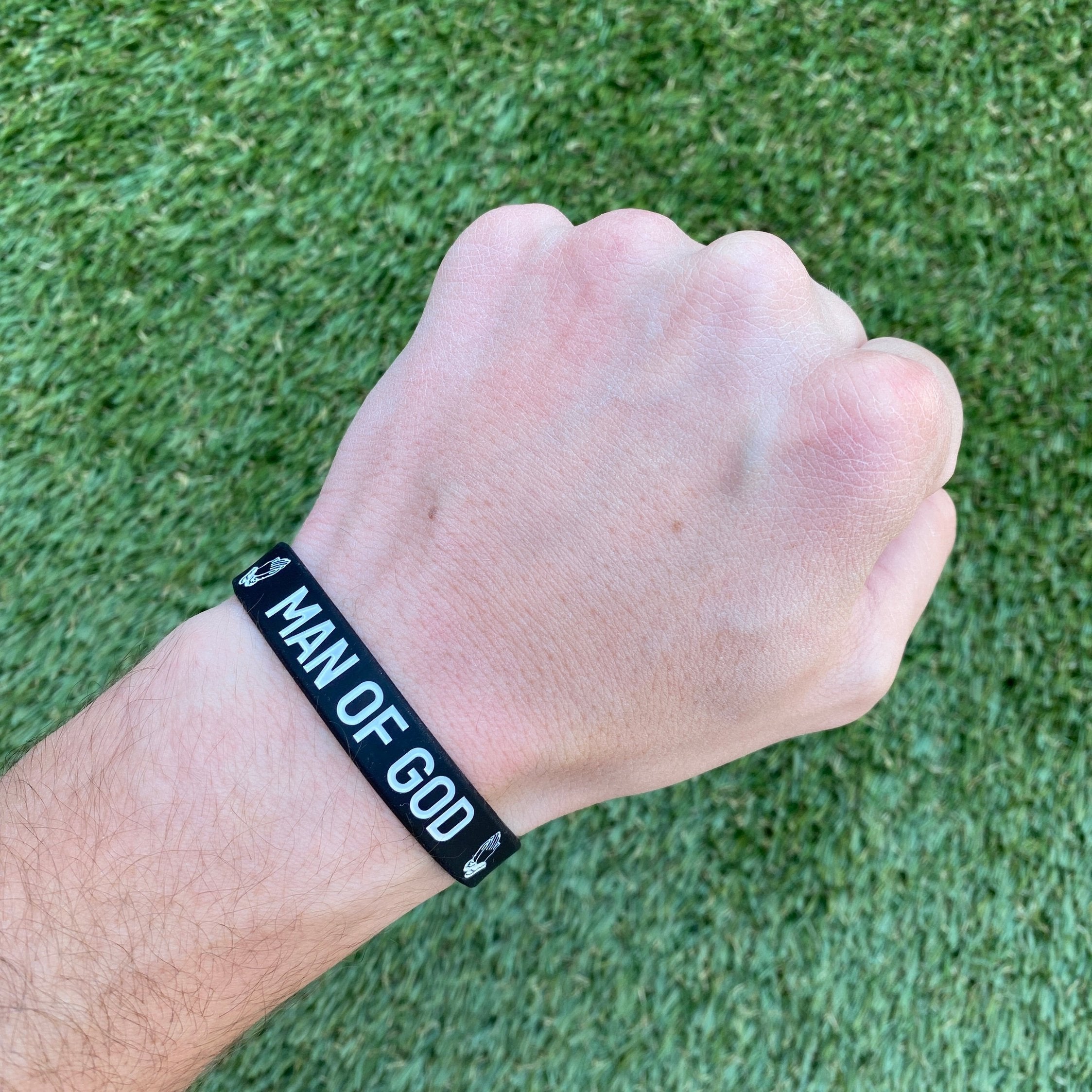 Collection of Hand wearing a black wristband with 'Man of God' text on a grass background in a gallery layout