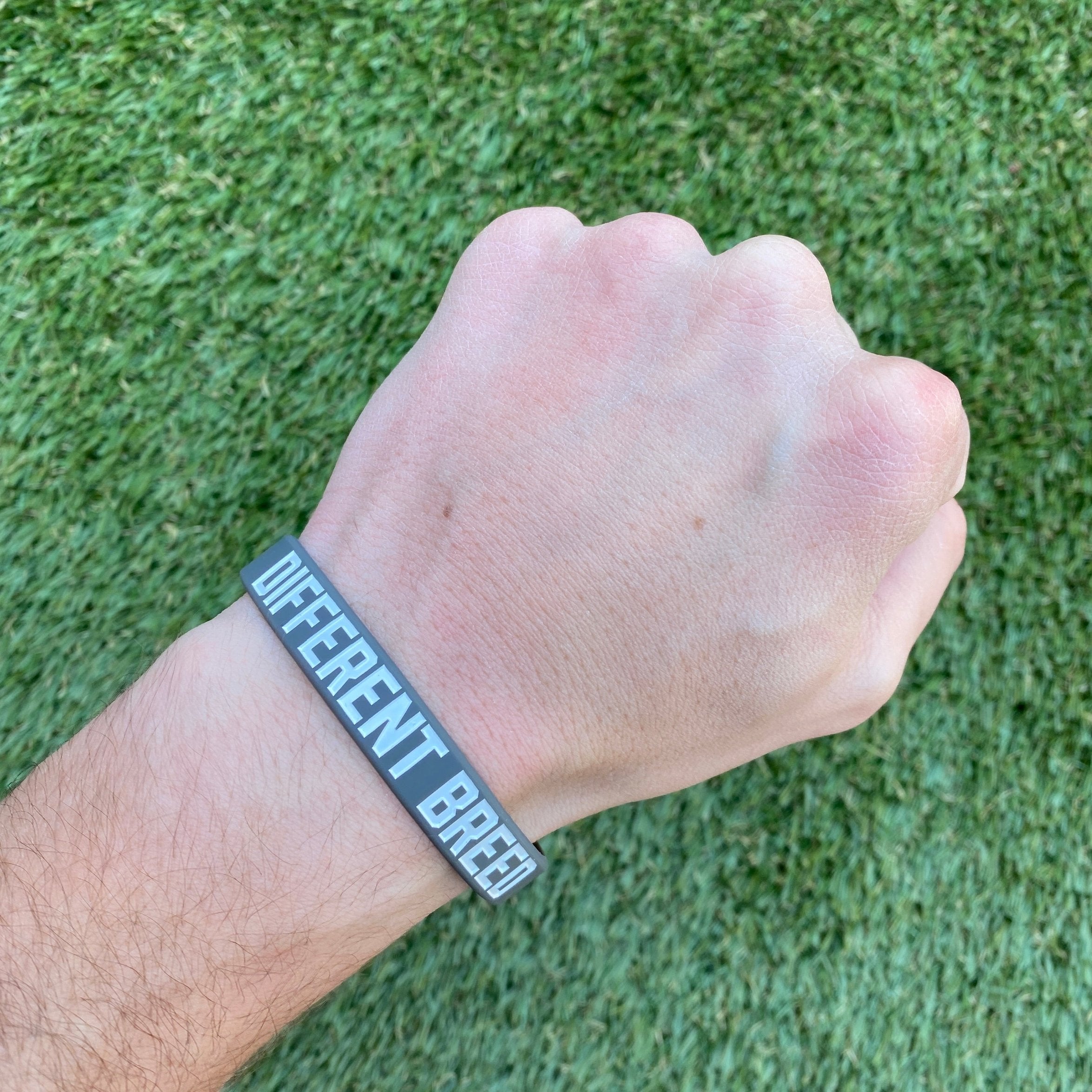 Collection of Hand wearing a wristband with 'Different Breed' text on a grass background in a gallery layout