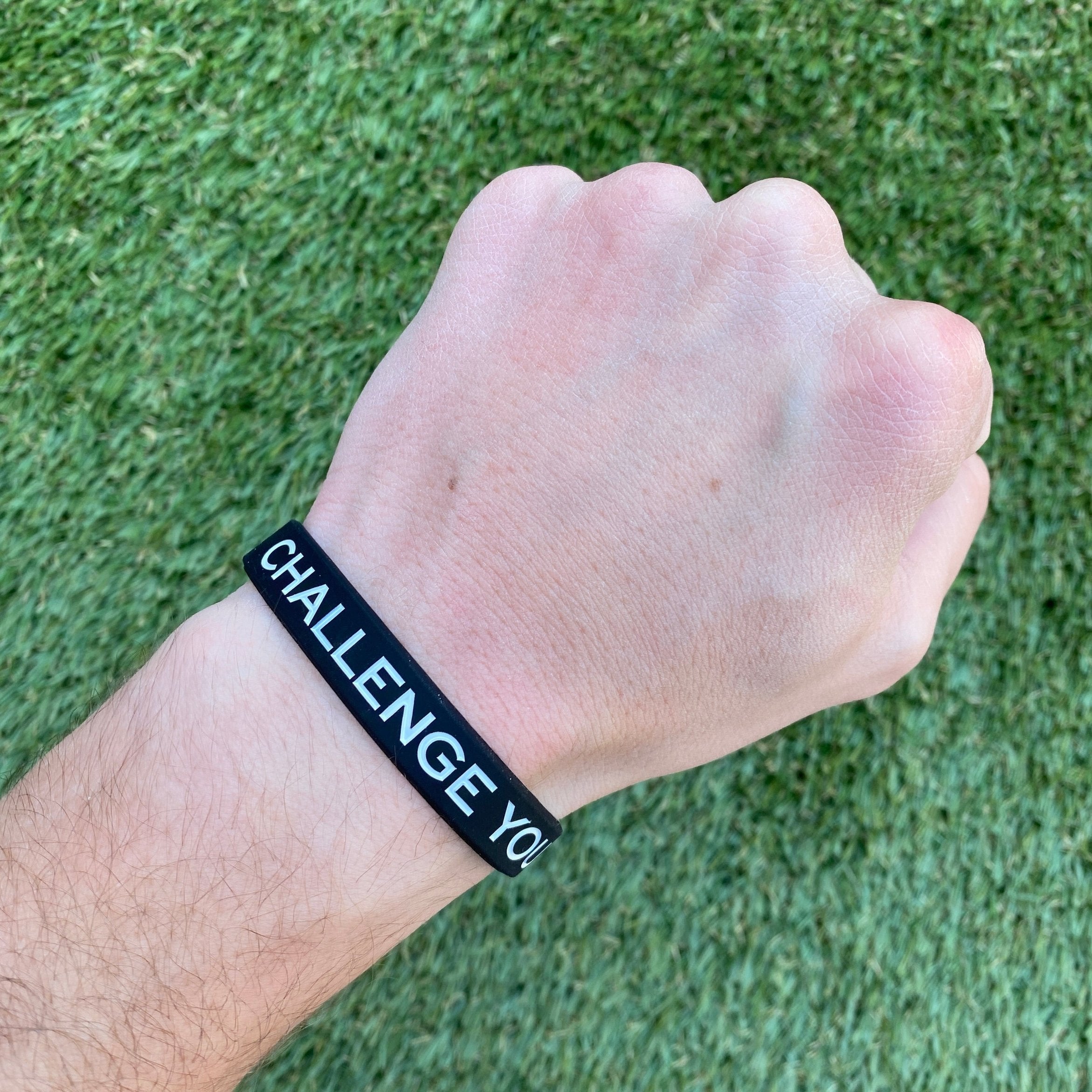 Collection of Hand wearing a black wristband with 'CHALLENGE YOU' text on a grass background in a gallery layout
