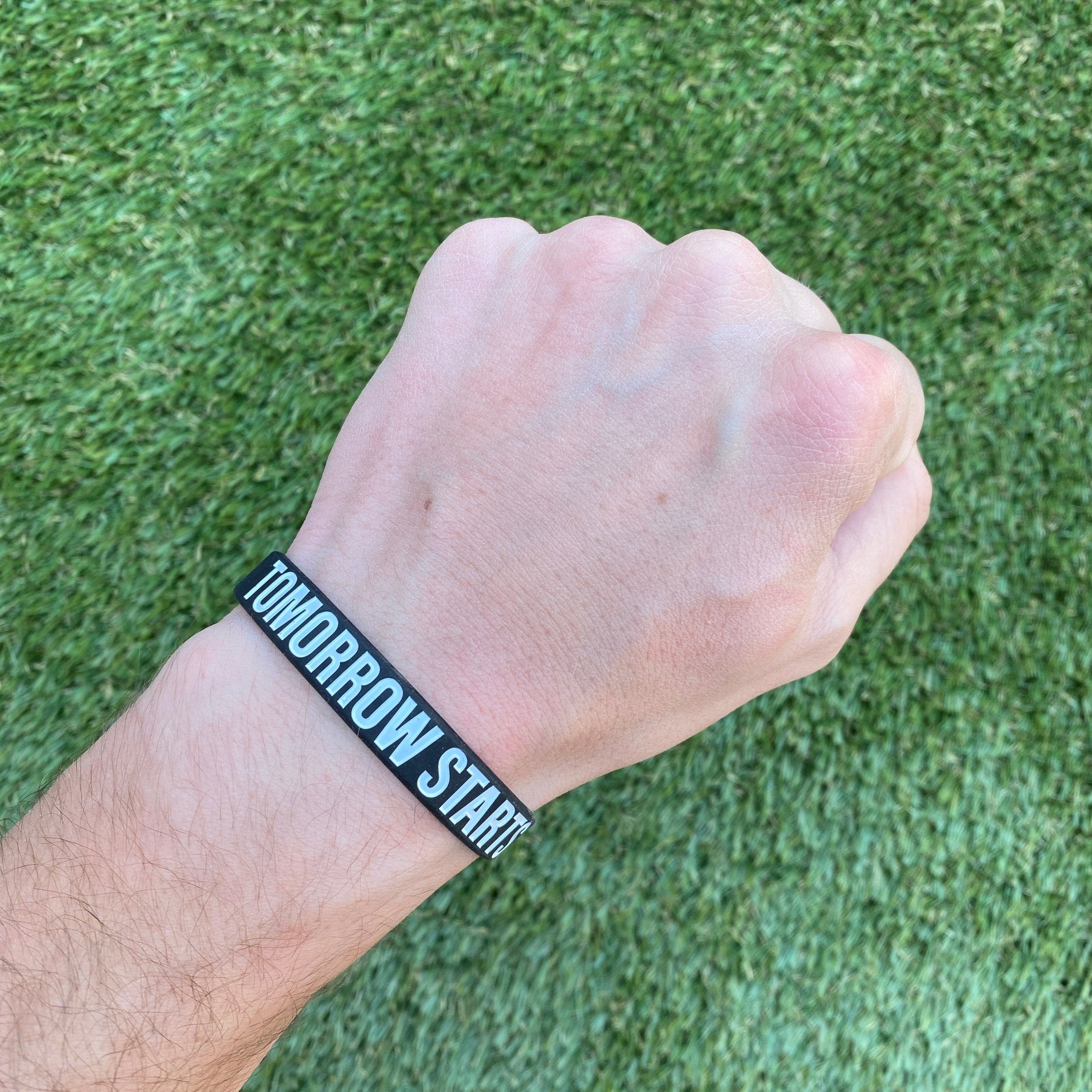 Collection of Hand wearing a black wristband with 'TOMORROW STARTS HERE' text on a grass background in a gallery layout
