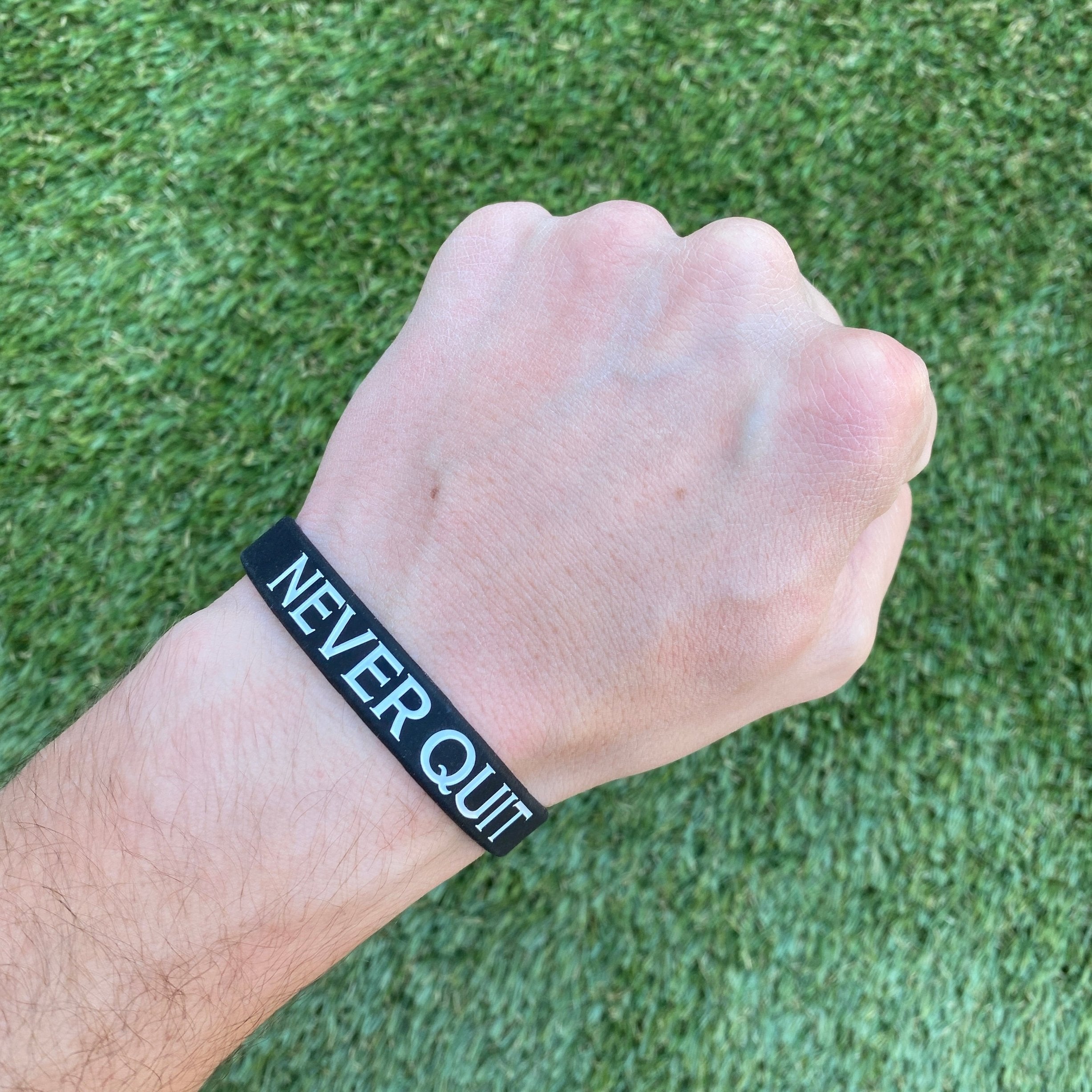 Collection of Hand wearing a 'Never Quit' wristband on a grass background in a gallery layout