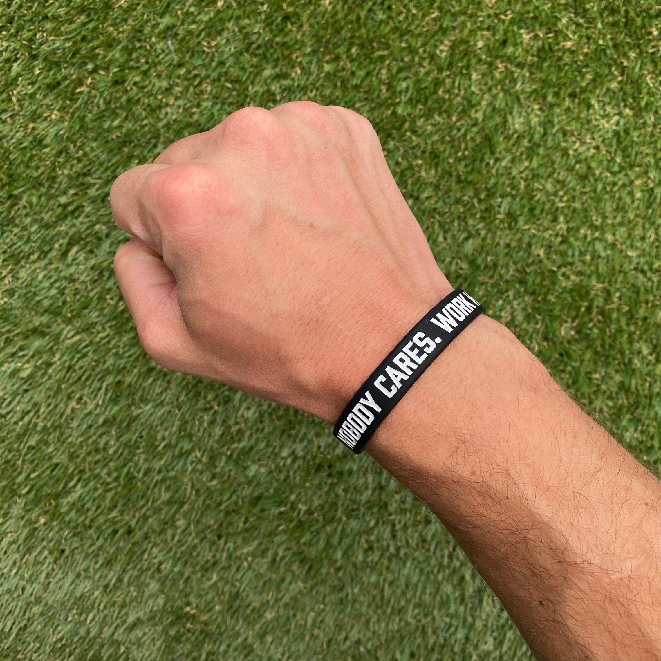 Collection of Hand wearing a black wristband with text on a grass background in a gallery layout