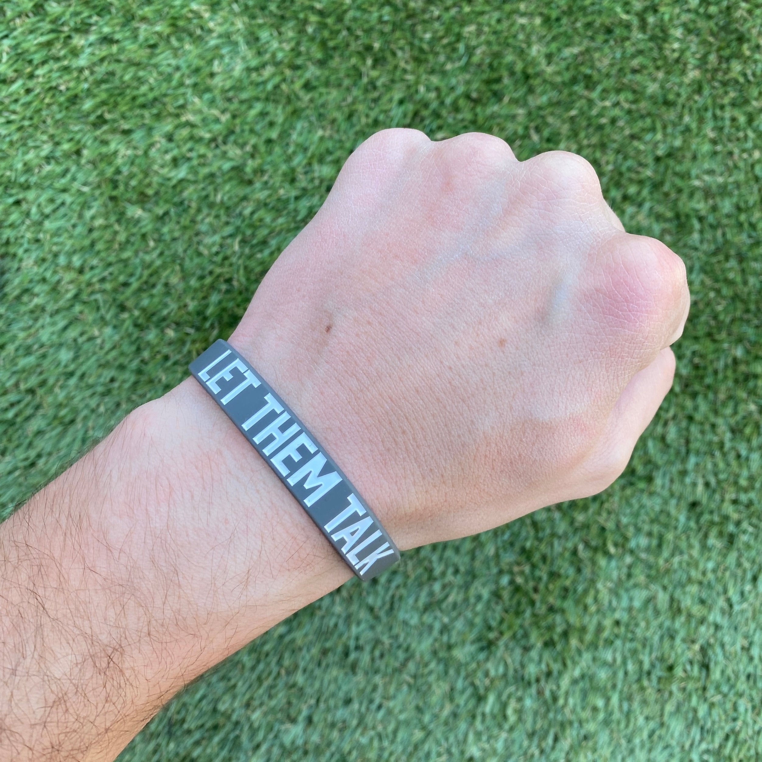 Collection of Wrist wearing a bracelet with 'LET THEM TALK' text on a grass background in a gallery layout