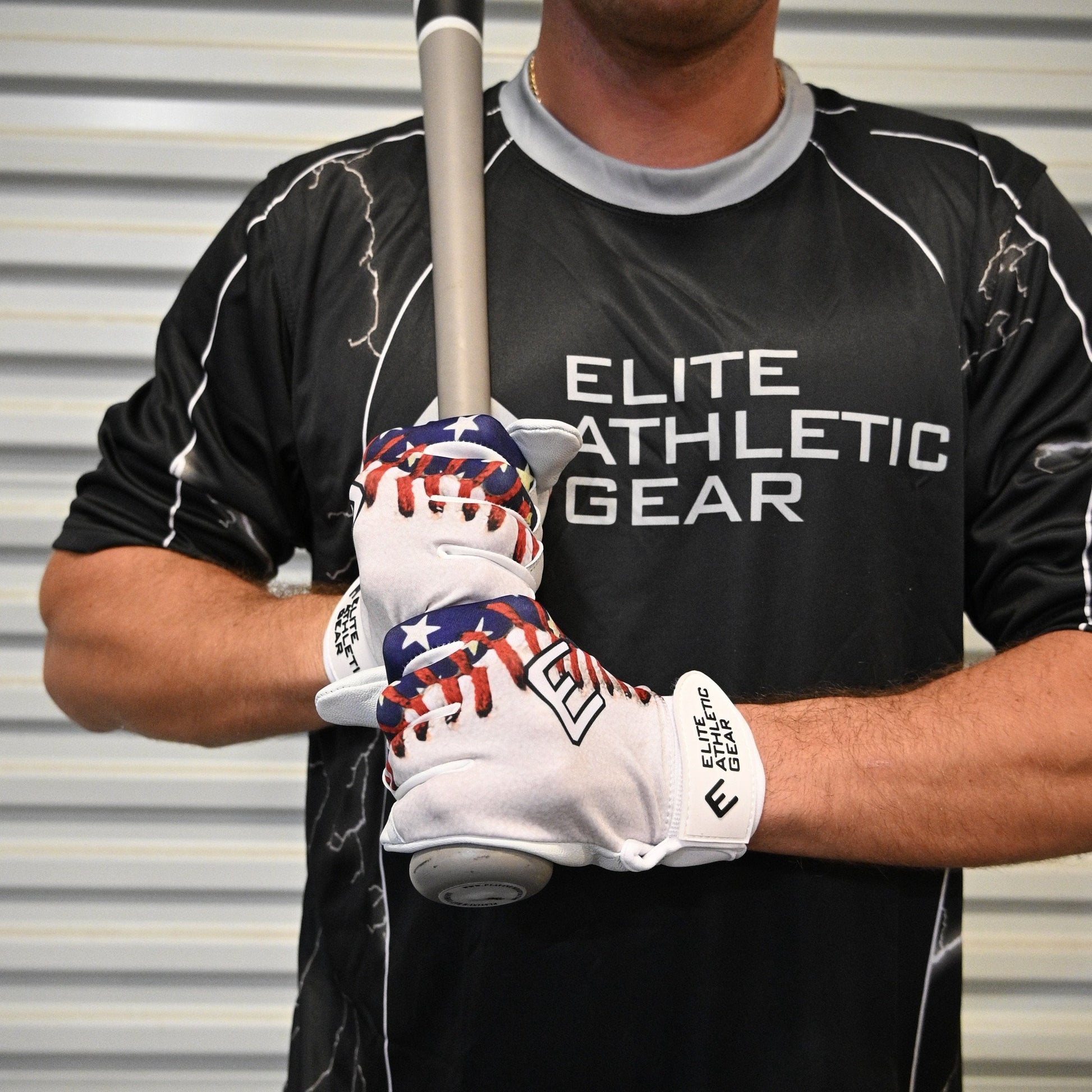 Person wearing a black 'Elite Athletic Gear' shirt and holding a baseball bat with gloves on.