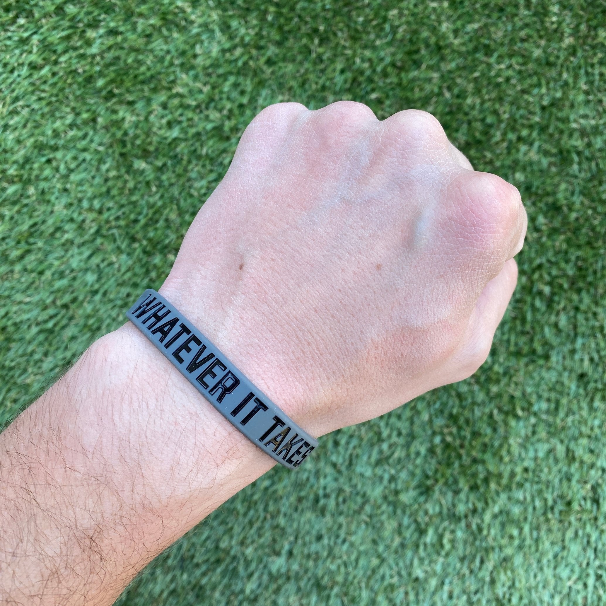 Collection of Hand wearing a wristband with 'Whatever It Takes' text on a grass background in a gallery layout