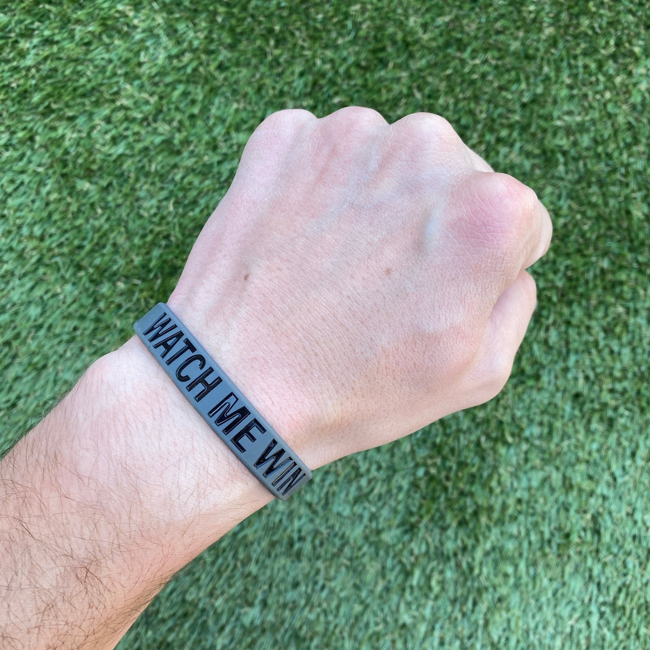 Collection of Hand wearing a black wristband with 'WATCH ME WIN' text on a grass background in a gallery layout