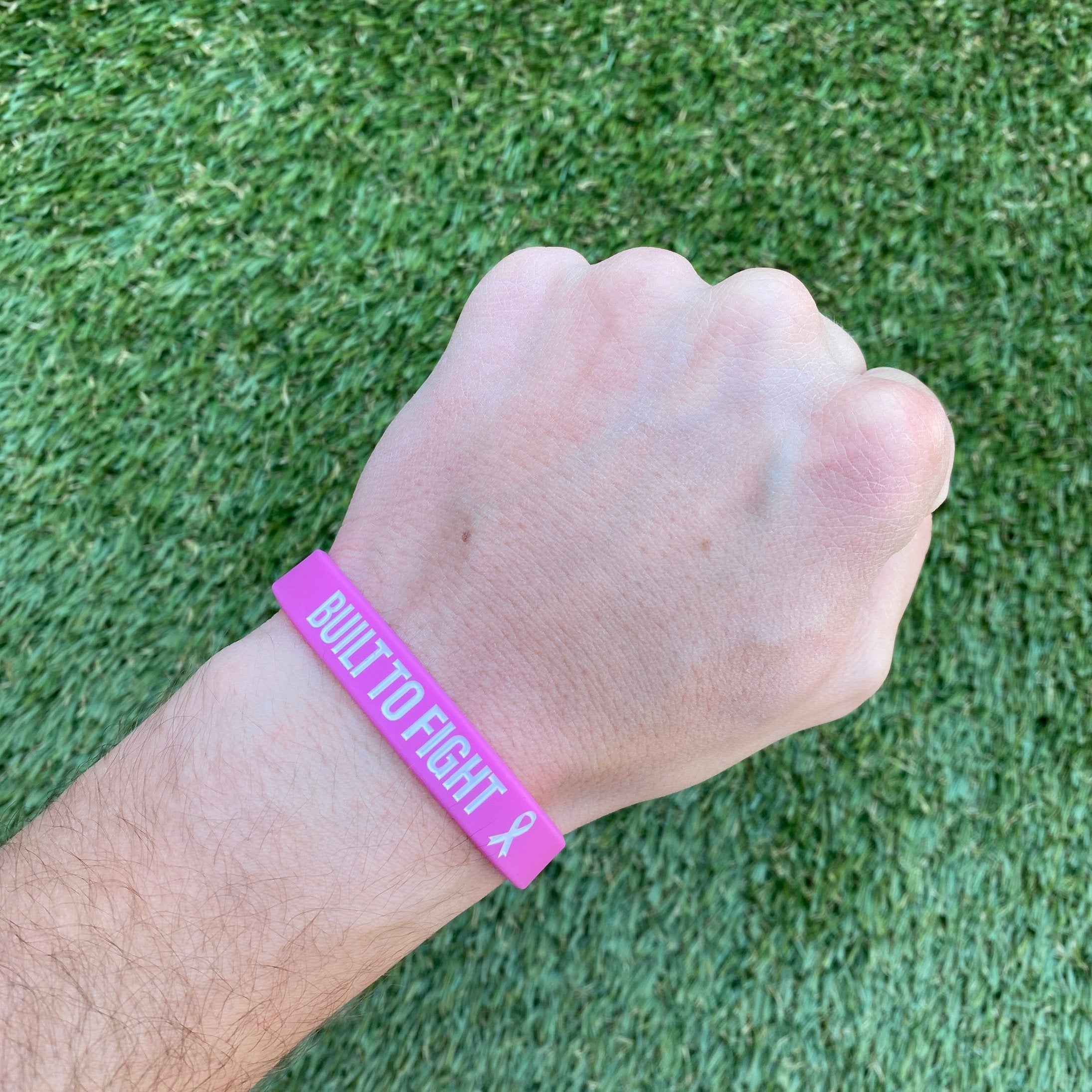 Collection of Hand wearing a pink wristband with 'BUILT TO FIGHT' text on grass background in a gallery layout