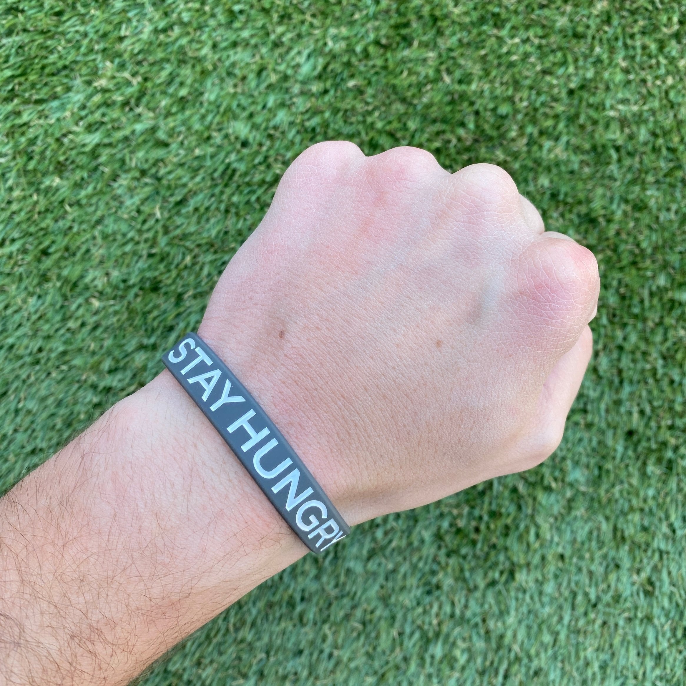 Collection of Hand wearing a wristband with 'STAY HUNGRY' text on a grass background in a gallery layout