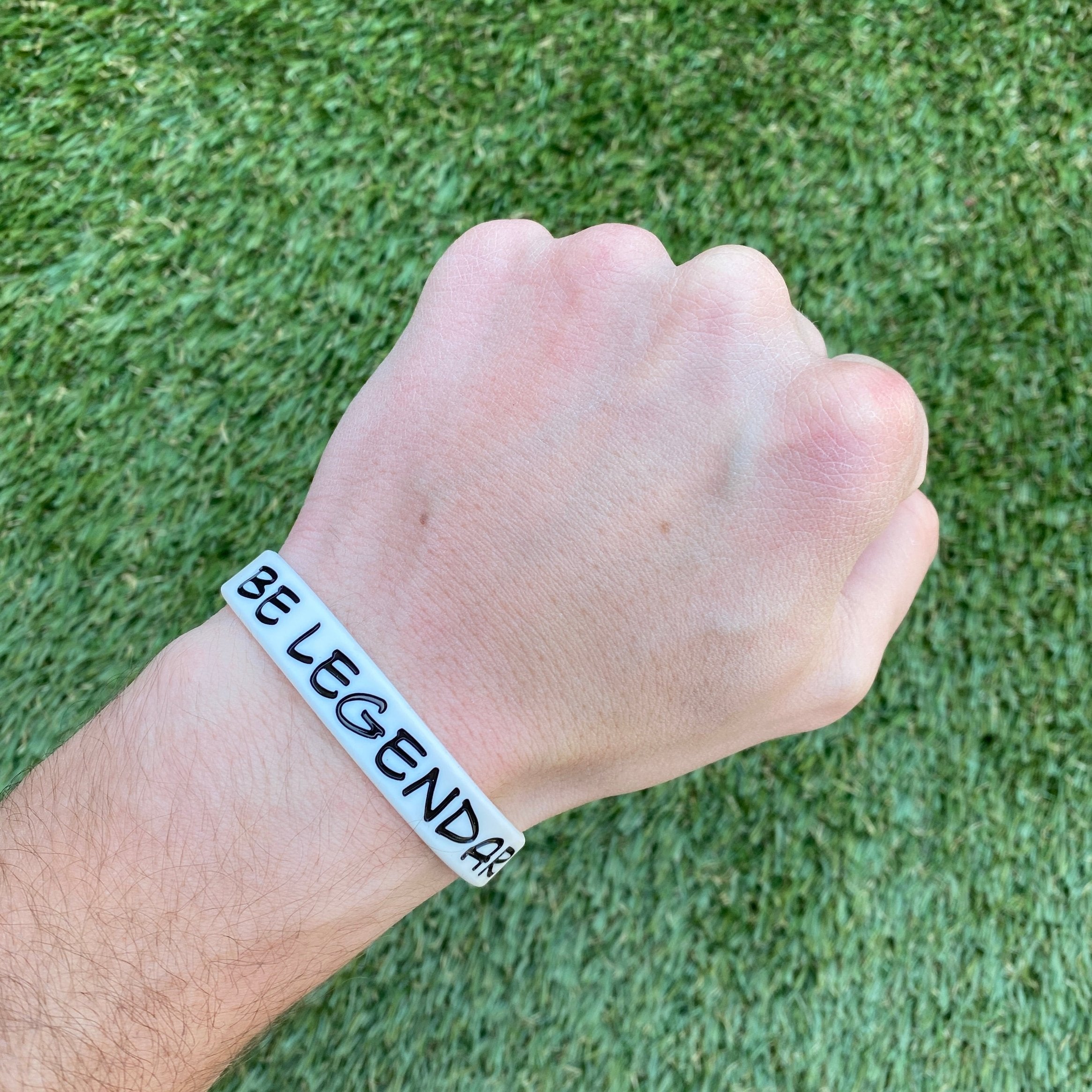 Collection of Hand wearing a bracelet with 'BE LEGENDARY' text on a grass background in a gallery layout