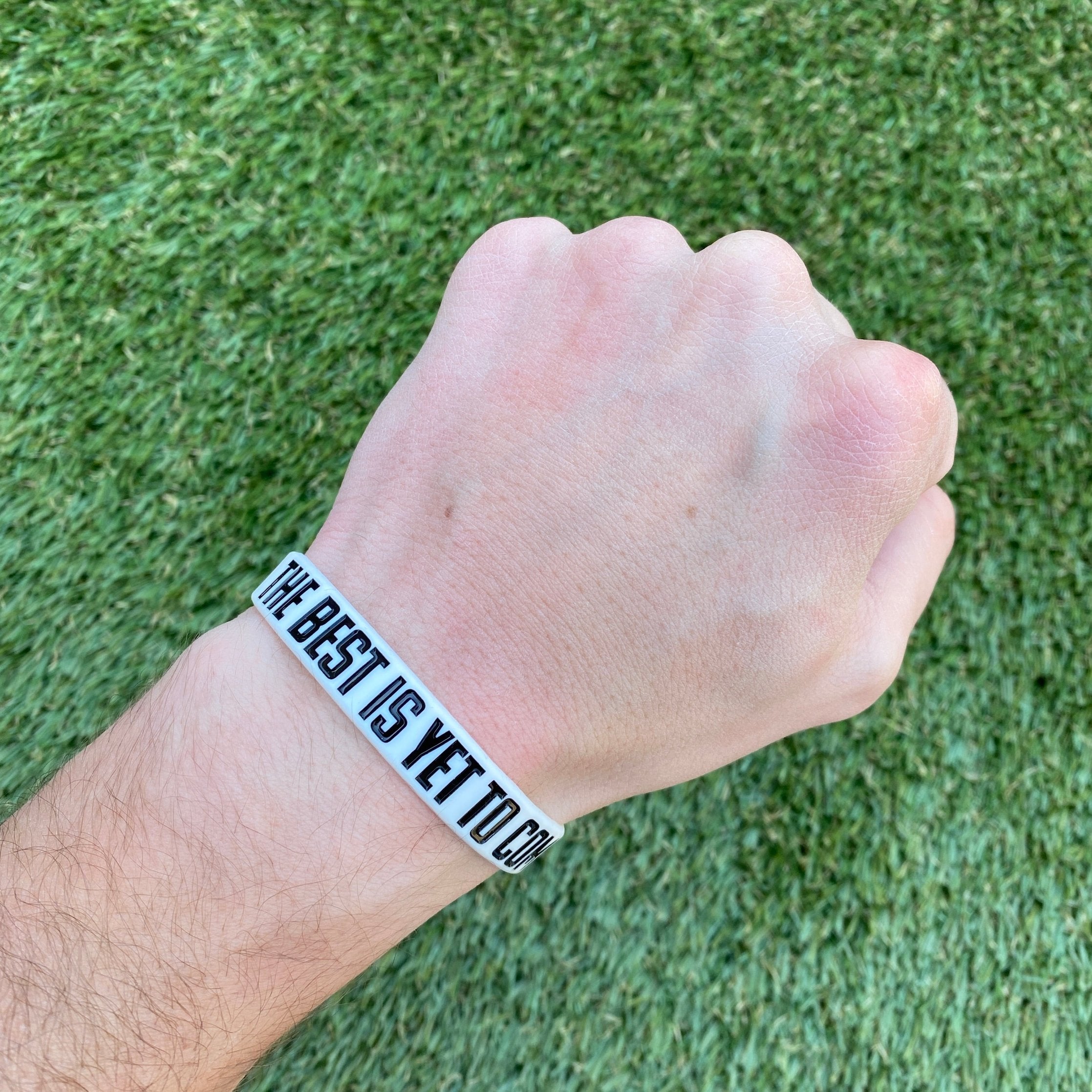Collection of Hand wearing a wristband with 'The Best is Yet to Come' text on a grass background in a gallery layout