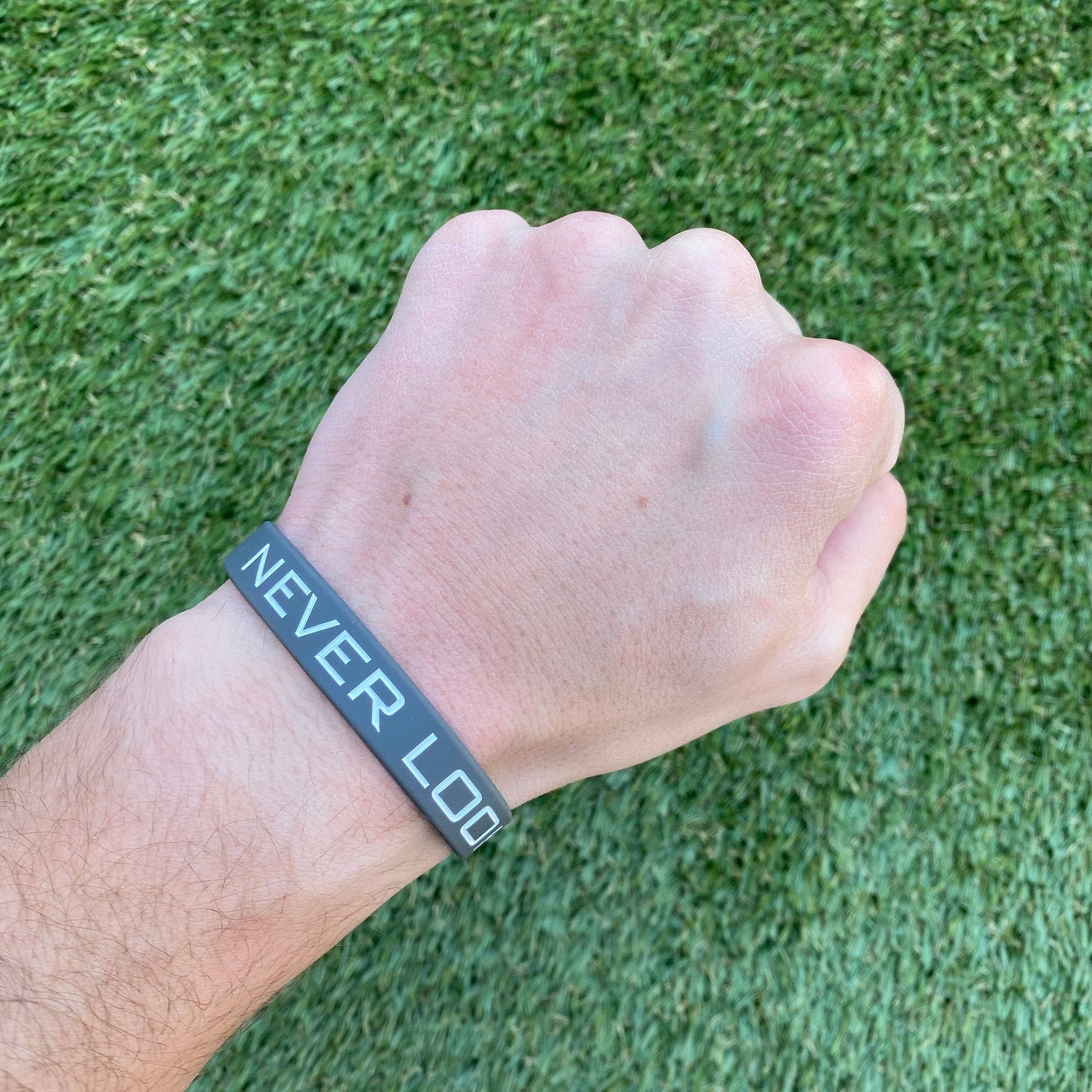 Collection of Hand wearing a wristband with 'NEVER LOSE' text on a grass background in a gallery layout