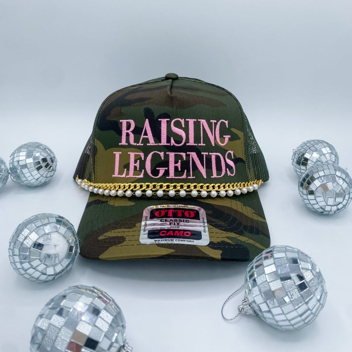 Collection of Camouflage cap with 'Raising Legends' text, surrounded by disco balls on a light gray background in a gallery layout